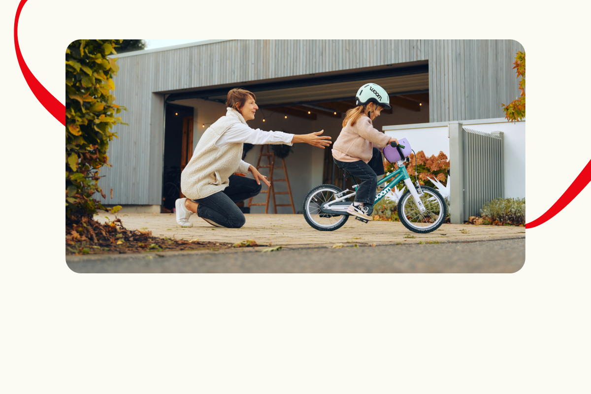 A family member supports a young girl as she enjoys her first moments with a new woom GO bike.