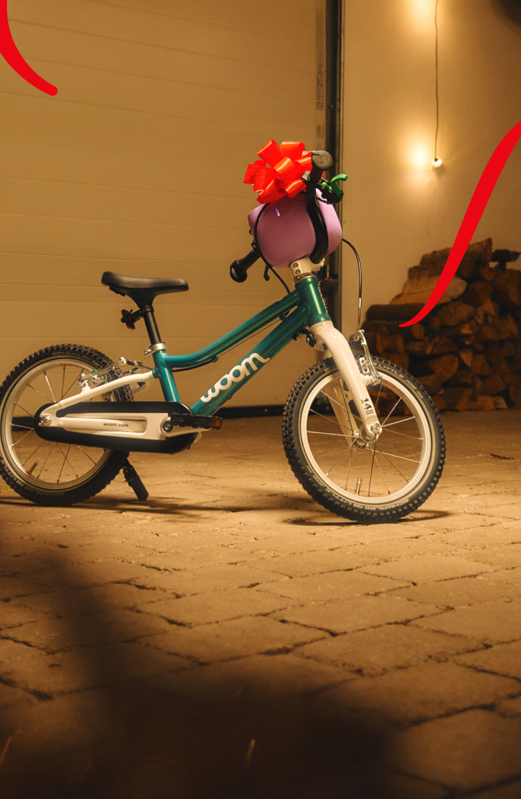 woom GO mit roter Schleife und POP Fahrradkorb, in einer gemütlichen, schwach beleuchteten Garage.