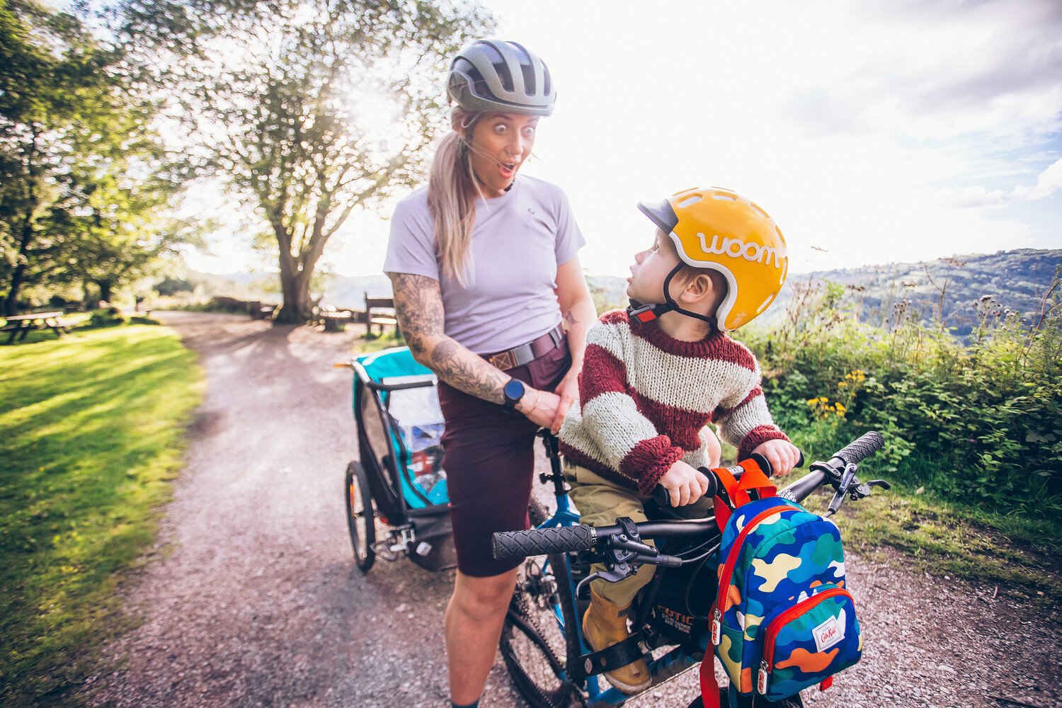 A young boy in a yellow woom helmet looks back at his mum from his seat on the front of her bike.