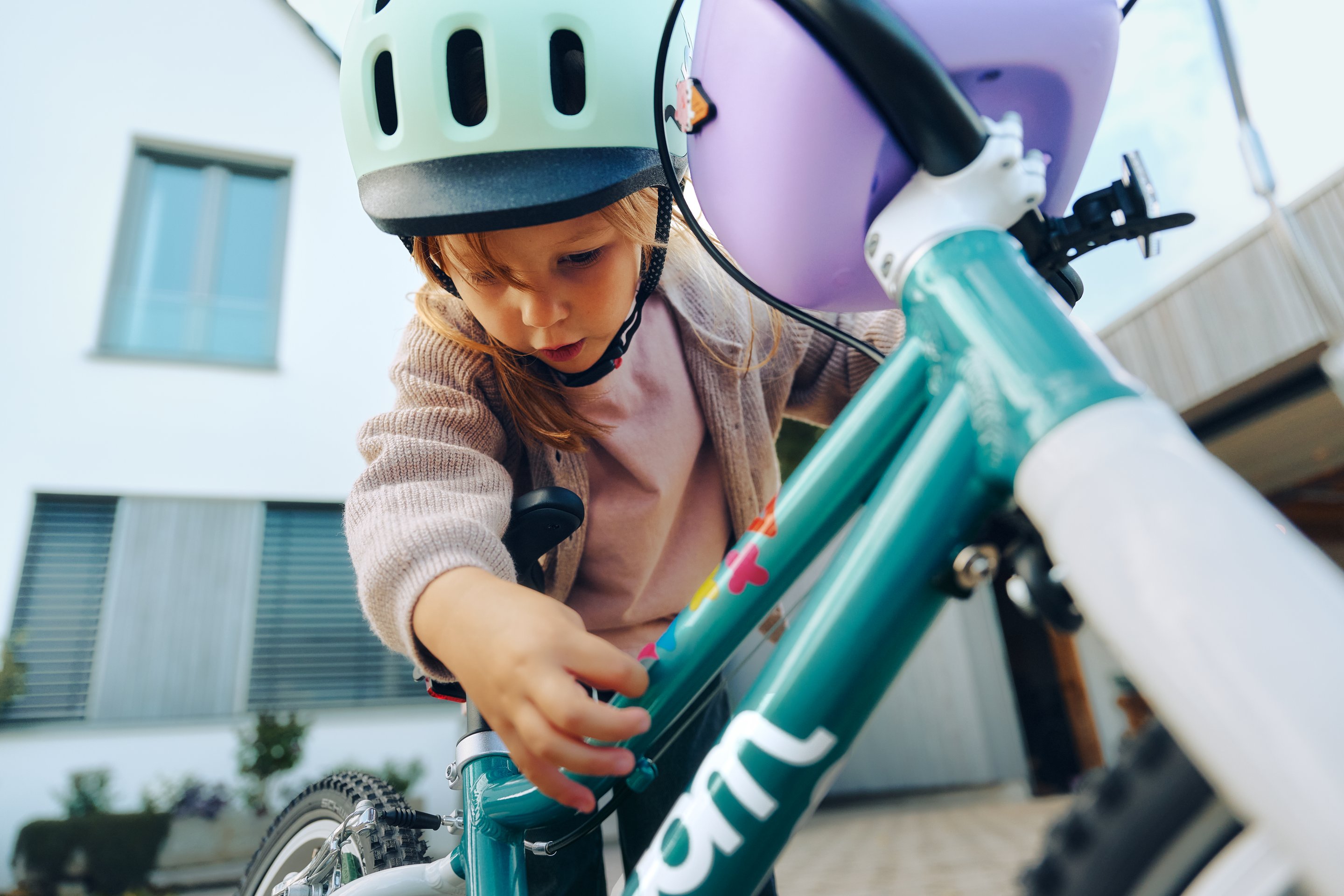 Child in a woom READY helmet in mint bends over their woom GO in metallic turquoise.