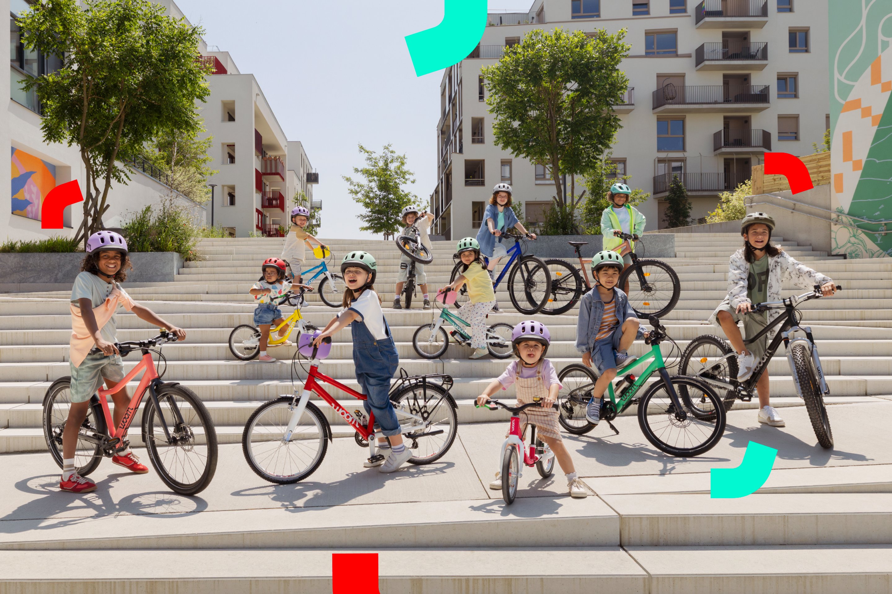 De nombreux enfants portant un casque enfant READY posent avec différents vélos woom sur des marches en dalles claires.