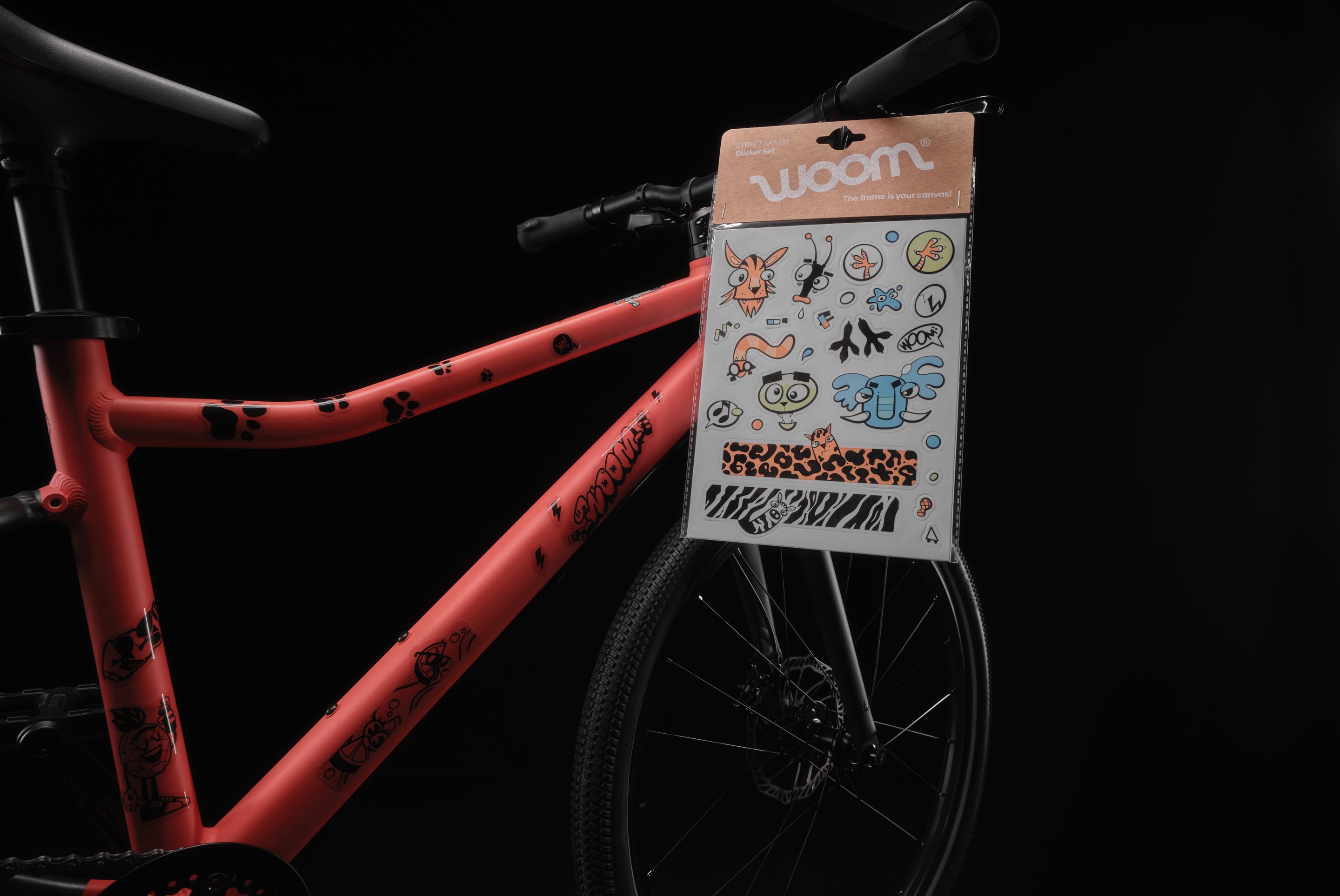 Vélo woom EXPLORE rouge avec un jeu d’autocollants Street Safari accroché au guidon.