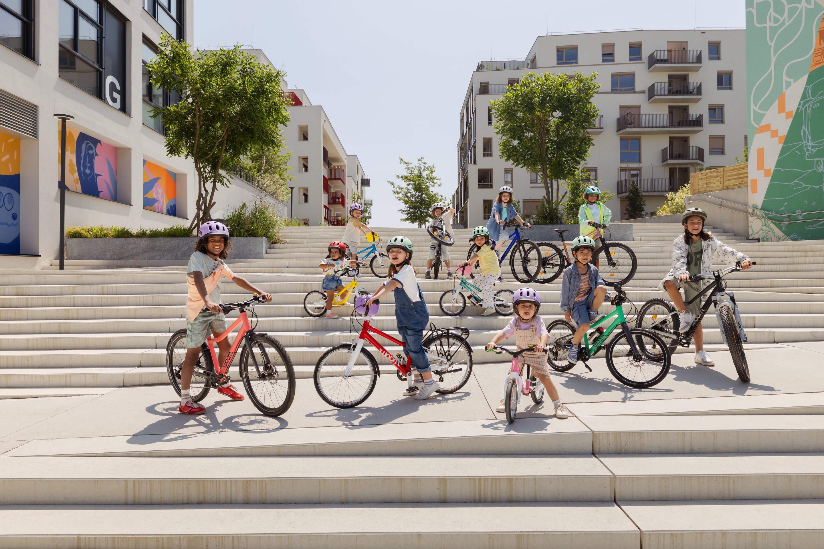 A group of children in woom READY kids helmets with various woom bikes, from a self-balancing bike to mountain bikes.