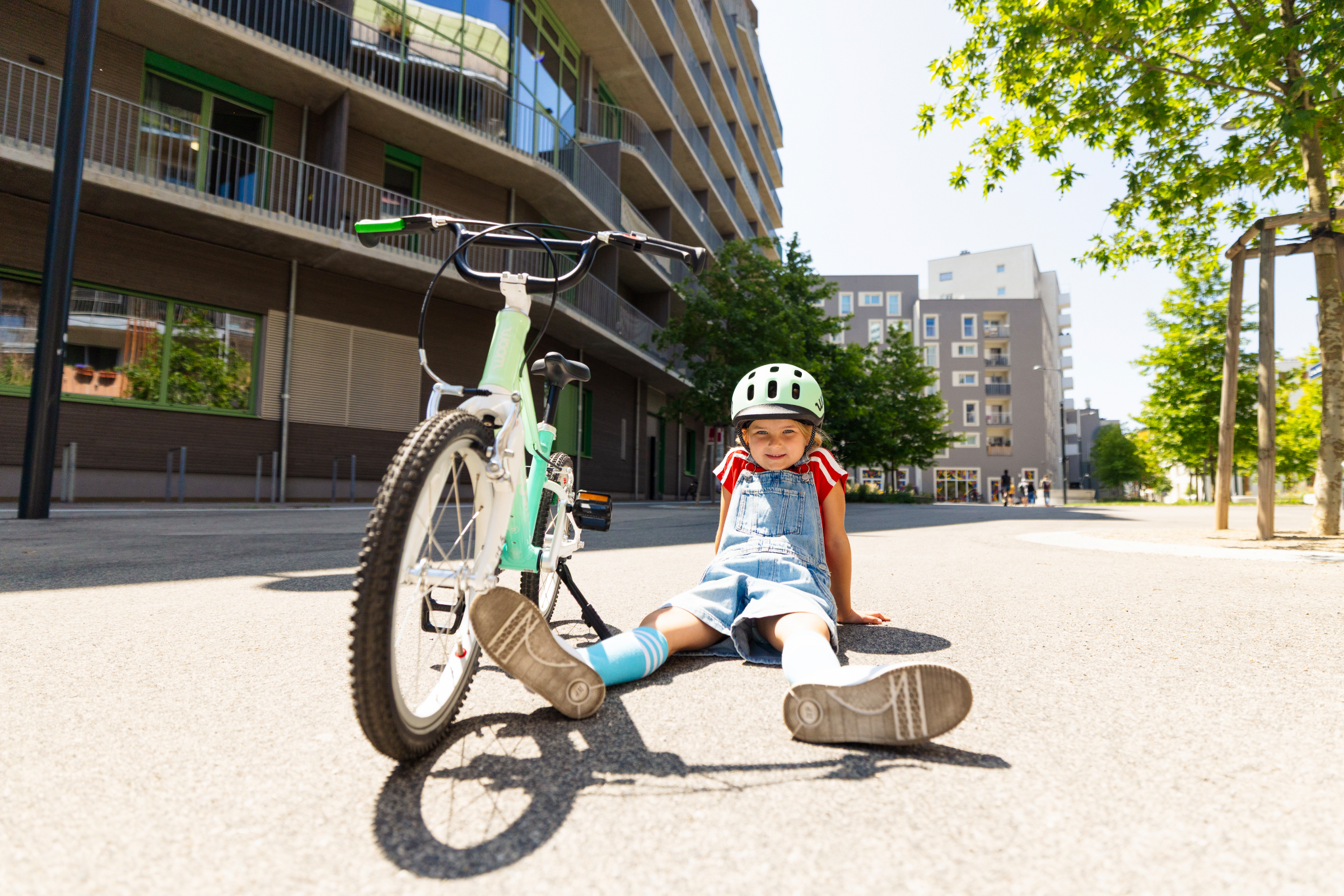 Child wearing a woom READY helmet sitting next to a spearmint crush woom GO bike on a sunny plaza.