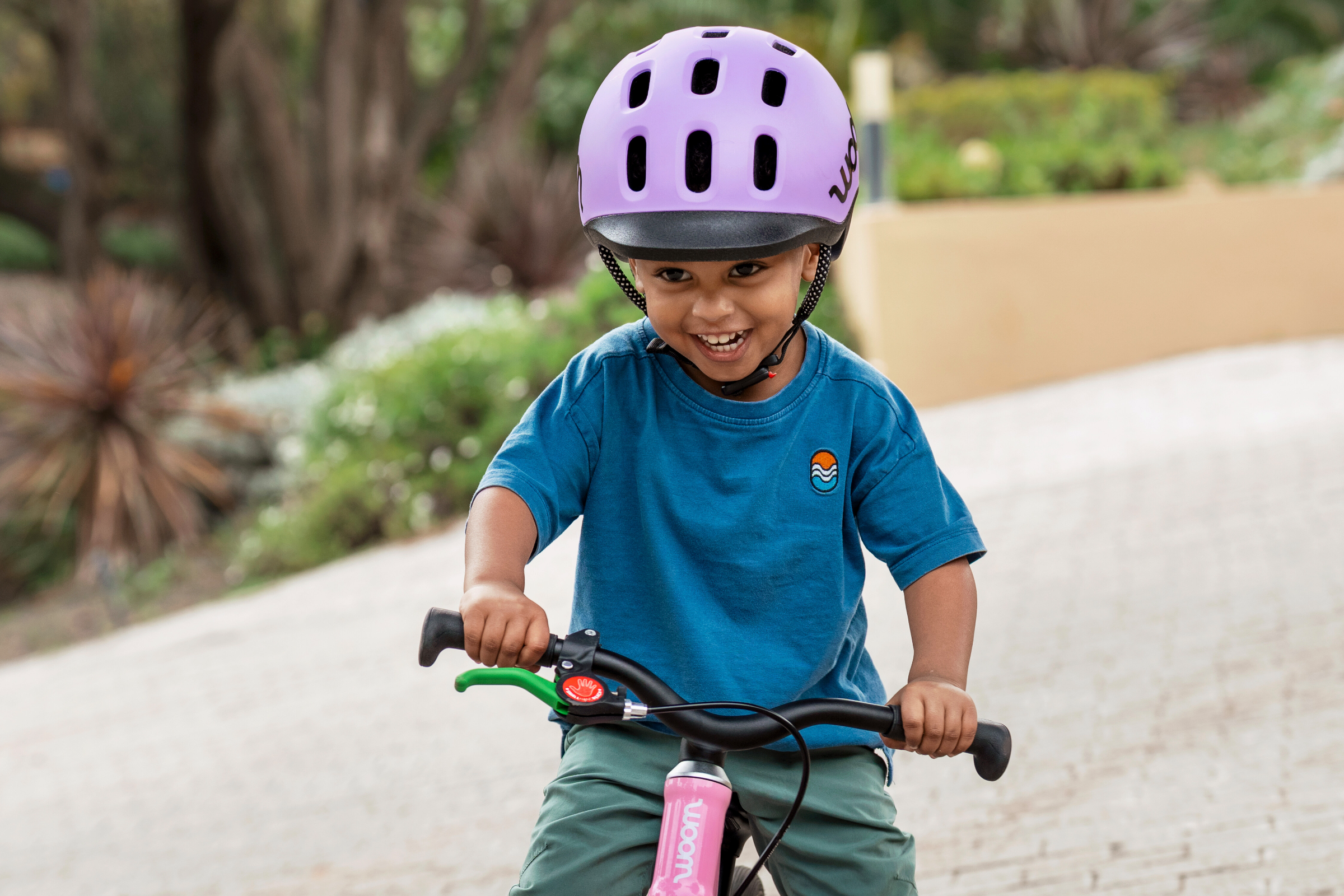 Smiling child with a purple READY helmet on a pink woom GO balance bike.