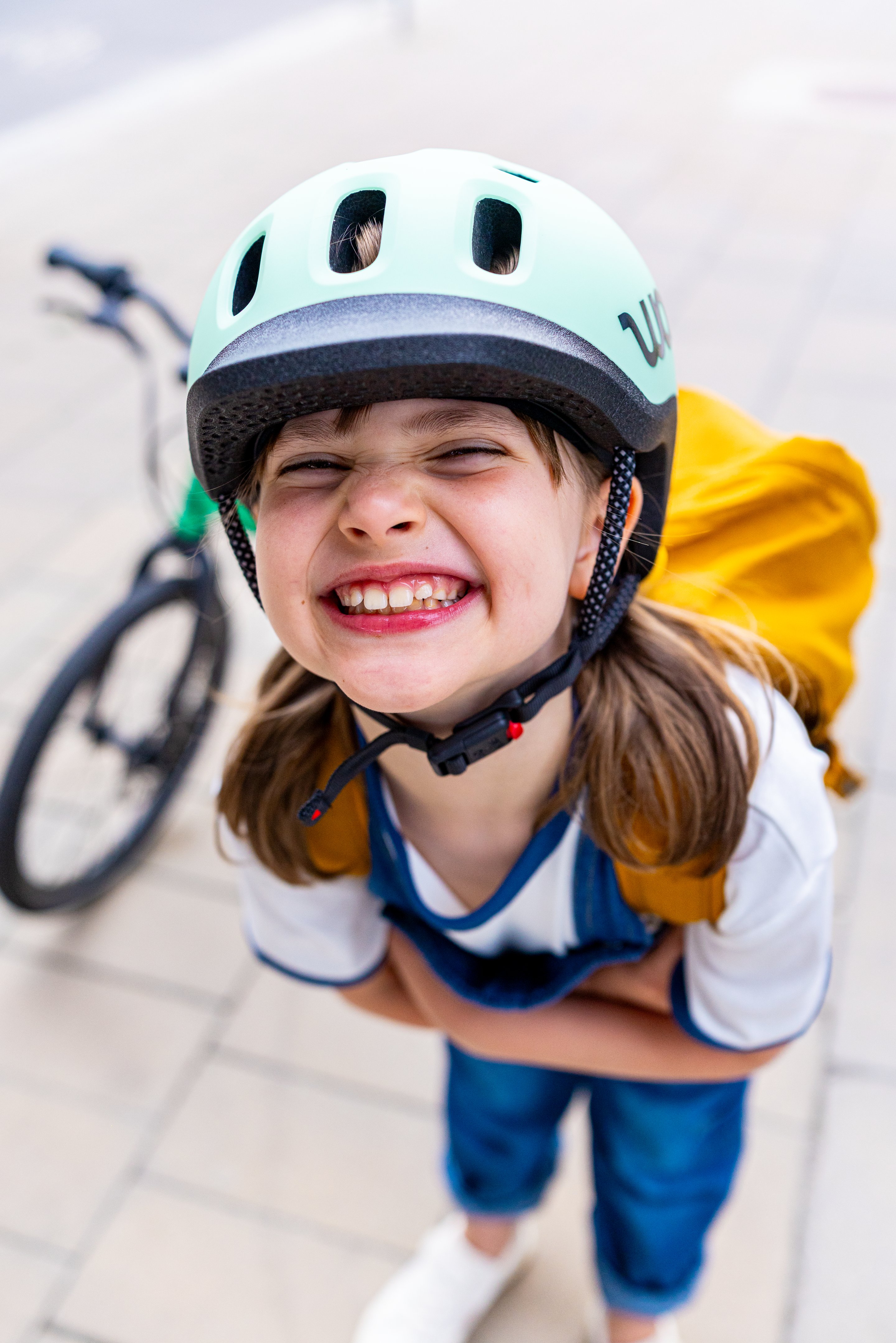 A girl wearing her woom READY Helmet and a backpack stands next to her woom EXPLORE bike grinning up at the camera with arms crossed.