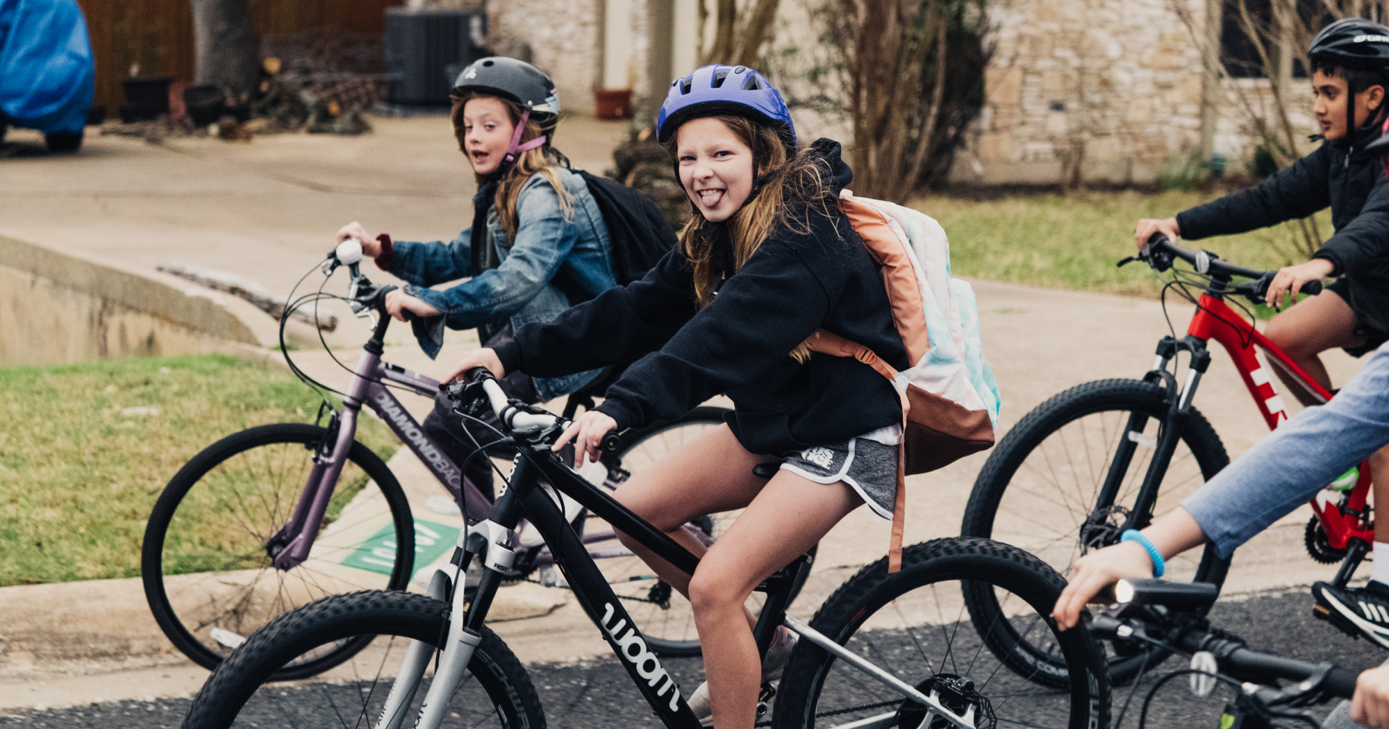 A girl on a woom OFF bike makes a silly face at the camera amidst a crowd of focused kids.