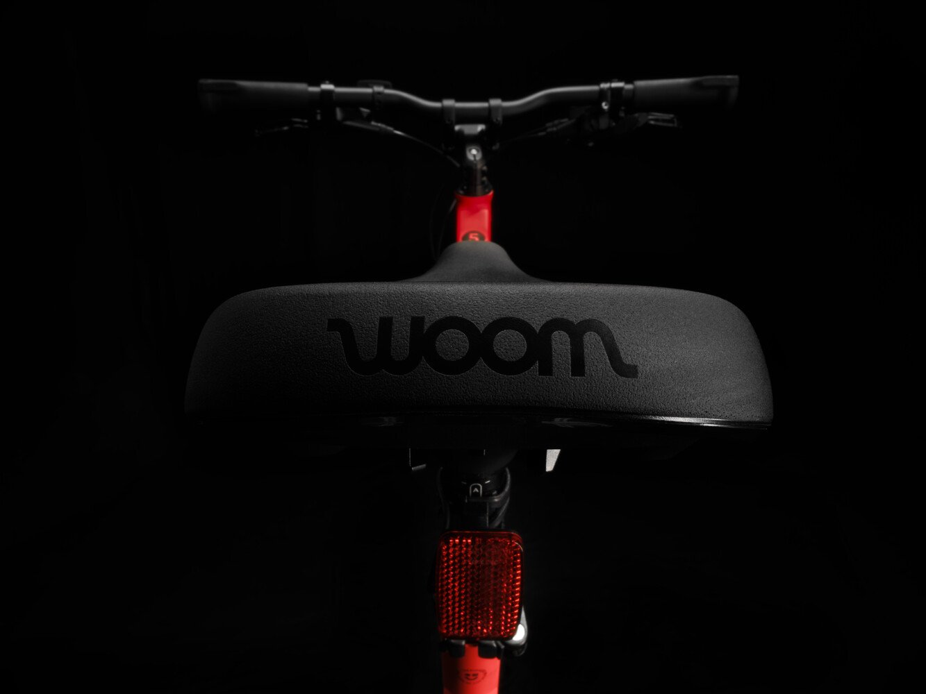 Gros plan sur la selle noire du vélo enfant woom EXPLORE avec le logo woom gravé au dos.