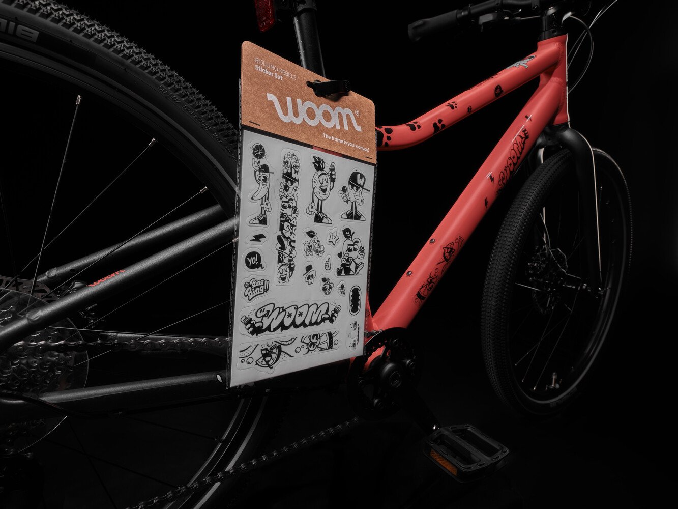 Een rood woom EXPLORE-fietsframe dat met zwarte, doorzichtige stickers is versierd, met daarnaast een set kleurrijke stickers.