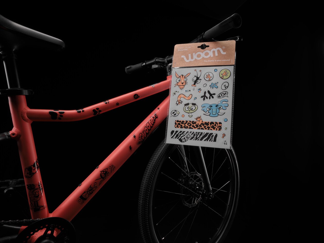 Een rood woom EXPLORE-fietsframe dat met zwarte, doorzichtige stickers is versierd, met daarnaast een set met kleurrijke stickers.