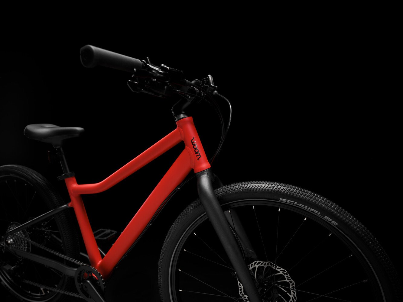 Side-on view of a woom EXPLORE children's bike with a red frame, black woom logo and black components.