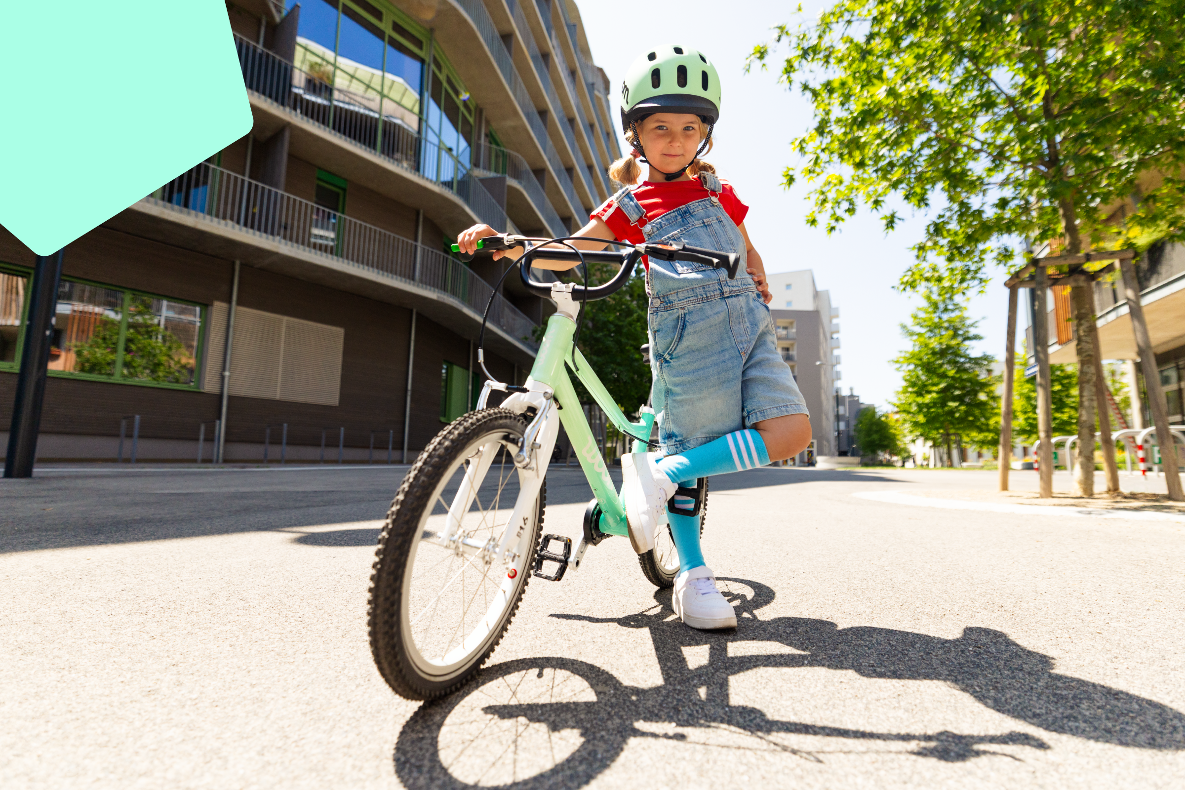 A girl in a mint green READY bicycle helmet stands casually with a limited edition spearmint crush woom GO children's bike.