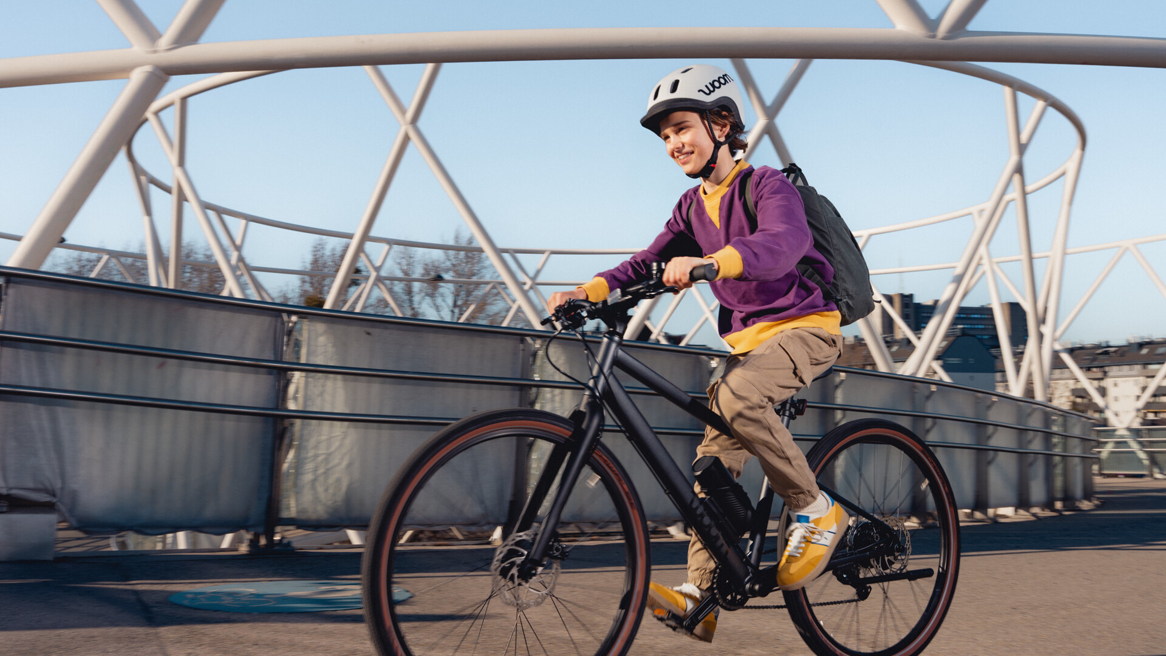 A boy wearing a purple sweatshirt is riding a woom EXPLORE e.
