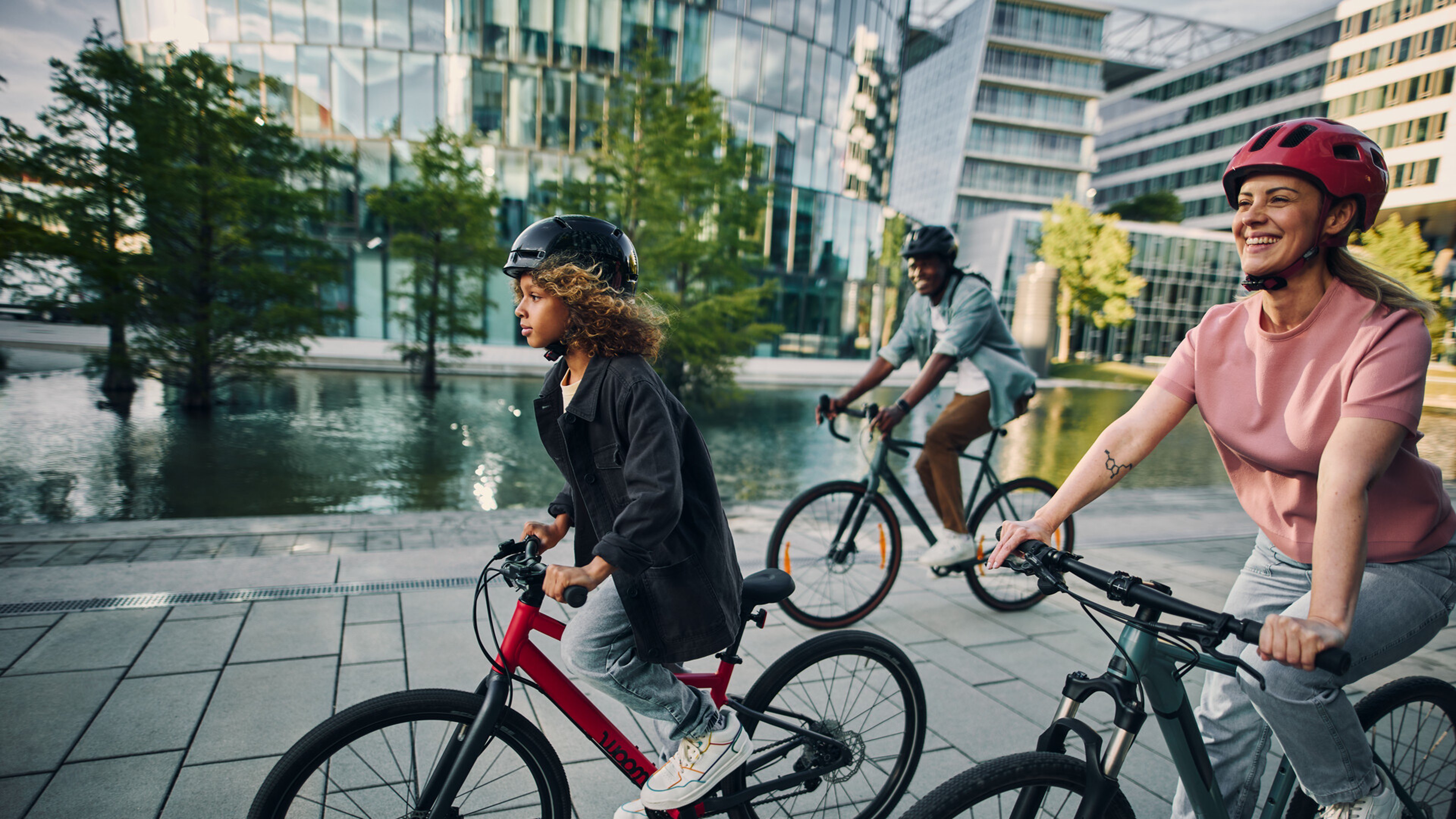 Un garçon traverse la ville sur un vélo rouge woom EXPLORE 5 de 24 pouces, accompagné de sa mère et de son père.