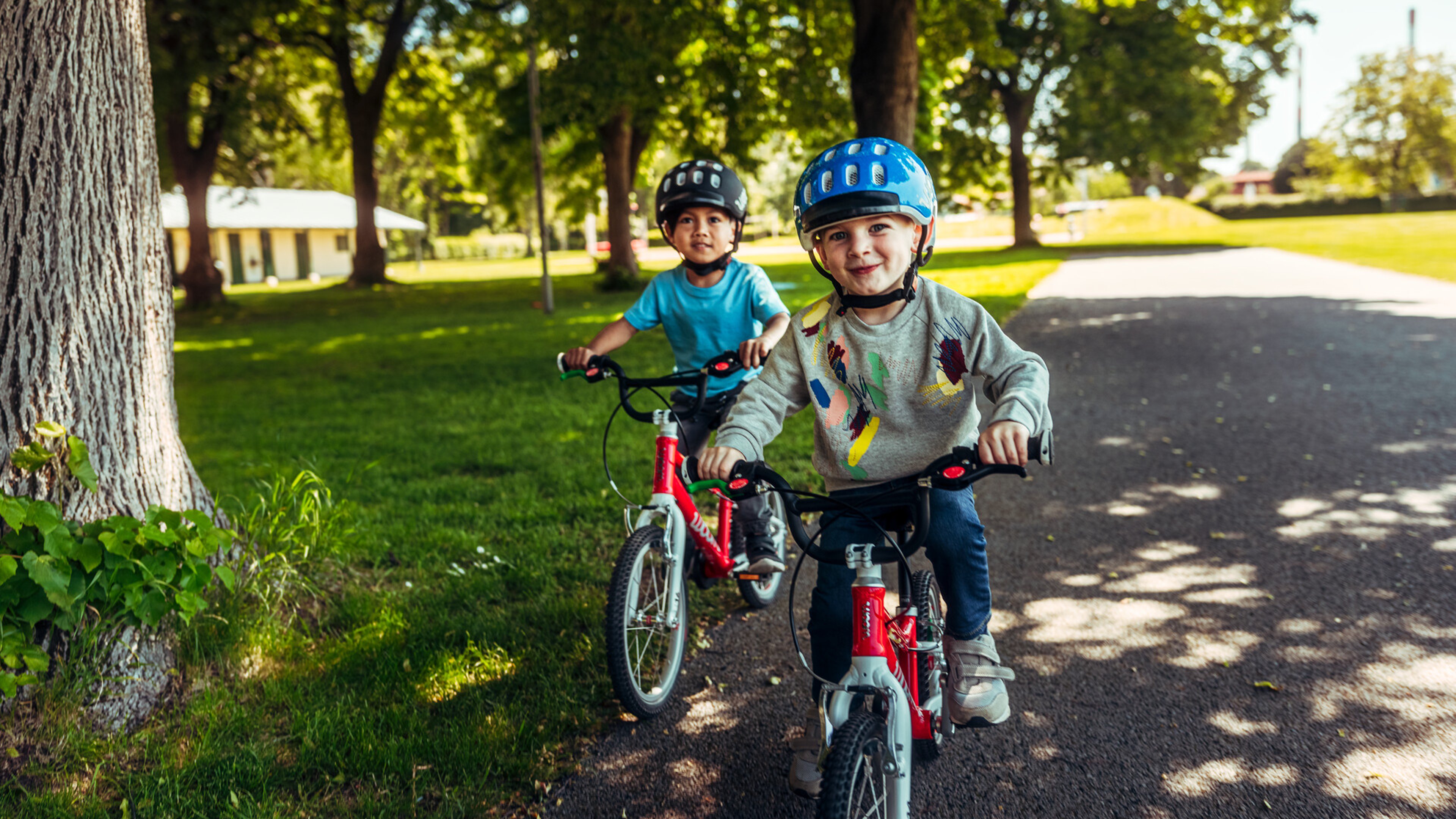 Two kids are wearing woom helmets and riding on red woom bikes.