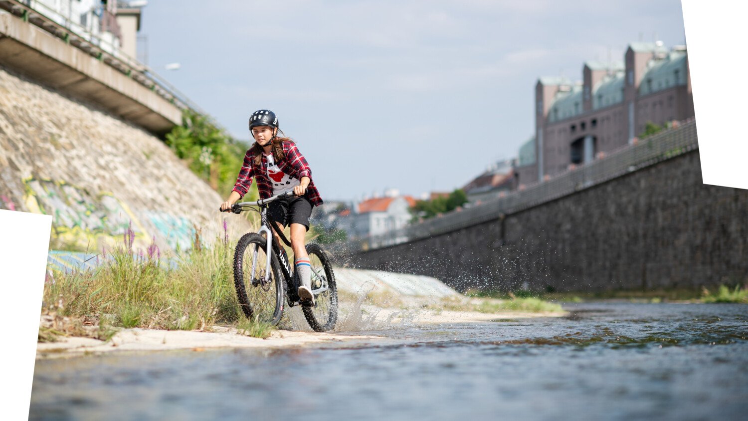 Kind mit schwarzem Radhelm auf dem Kopf fährt mit einem schwarzen woom OFF Mountainbike neben dem Wienfluss.