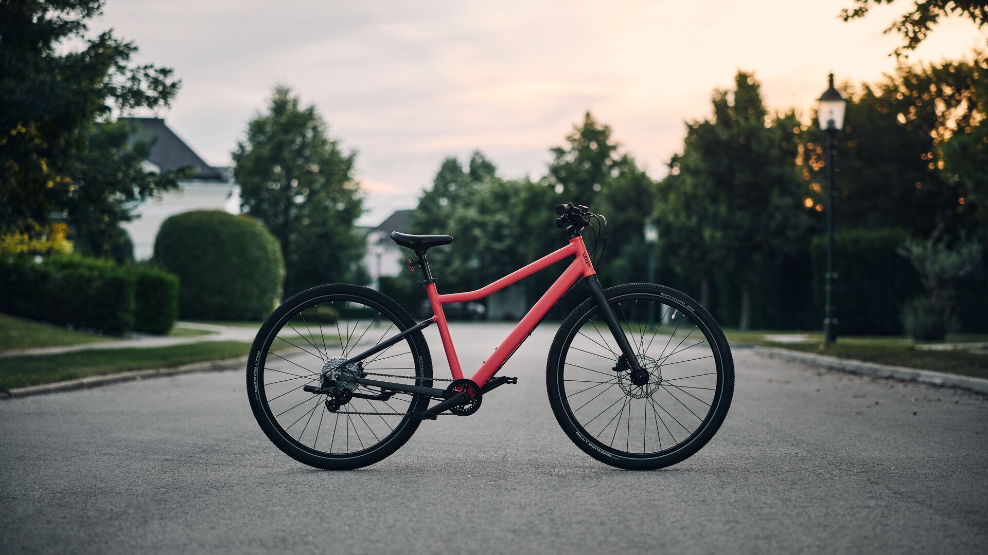 A red children's bike from woom stands upright on a suburban street.