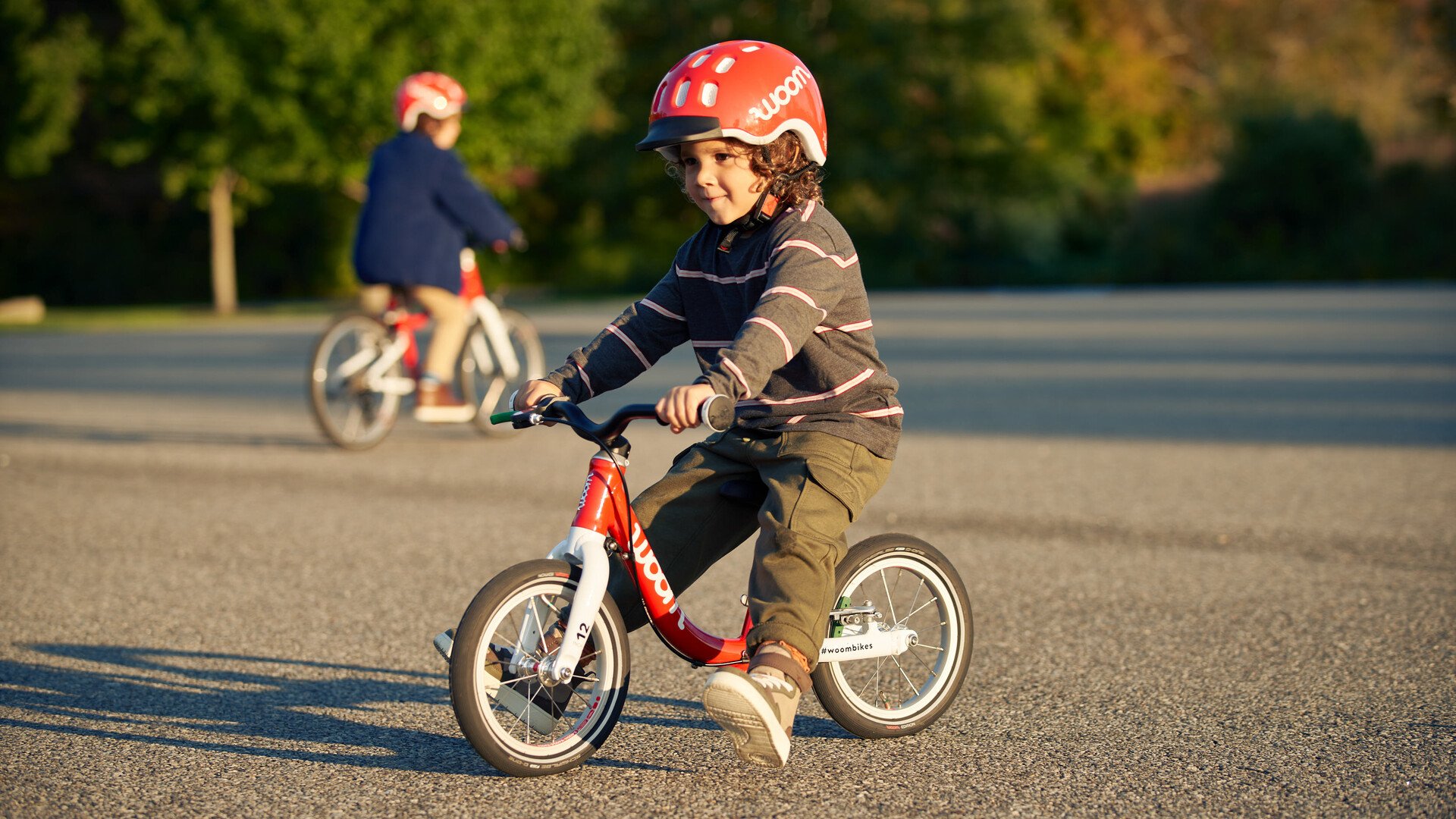 A child in red helmet rides along the tarmac on a red balance bike from the brand woom.