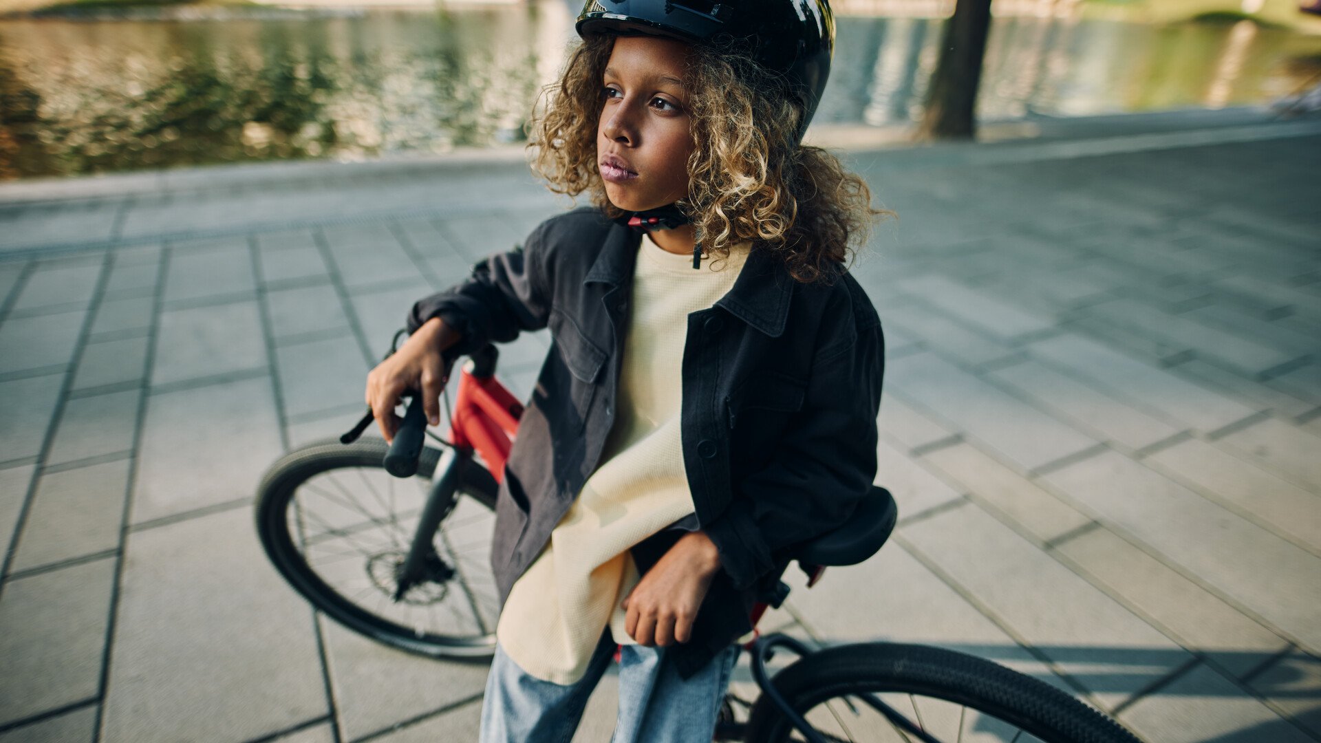 A boy is leaning against his red woom bike and looking thoughtfully into the distance.