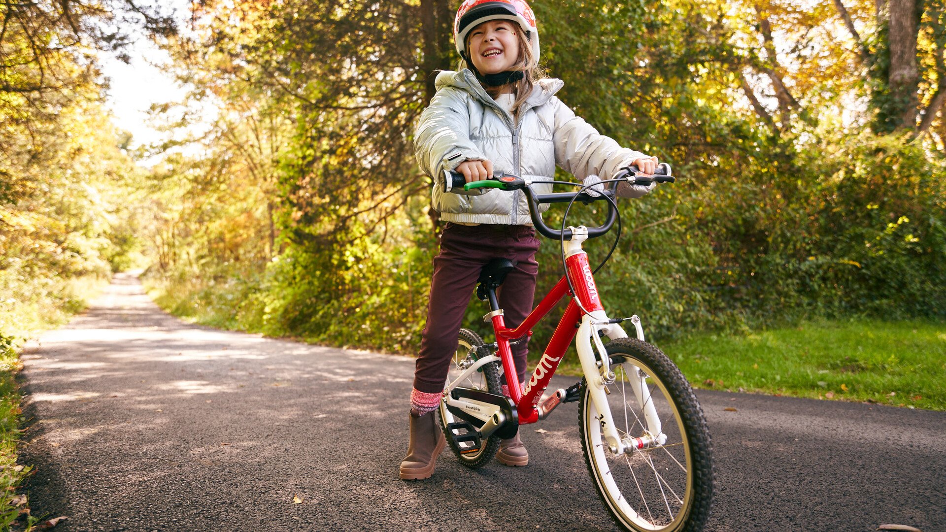 Une petite fille rayonne, tout sourire, sur son vélo enfant rouge de la marque woom.