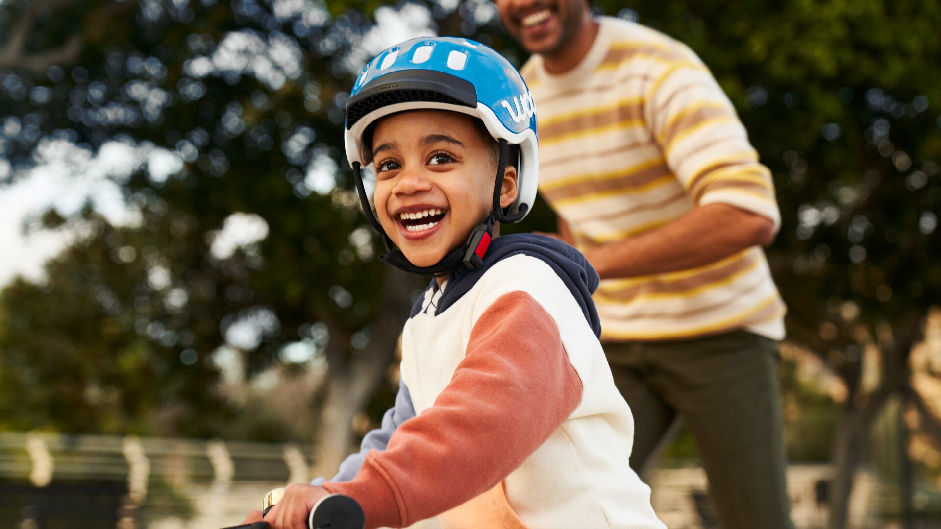 Un enfant sur son vélo avec un casque bleu de la marque woom sourit face à l’appareil photo.