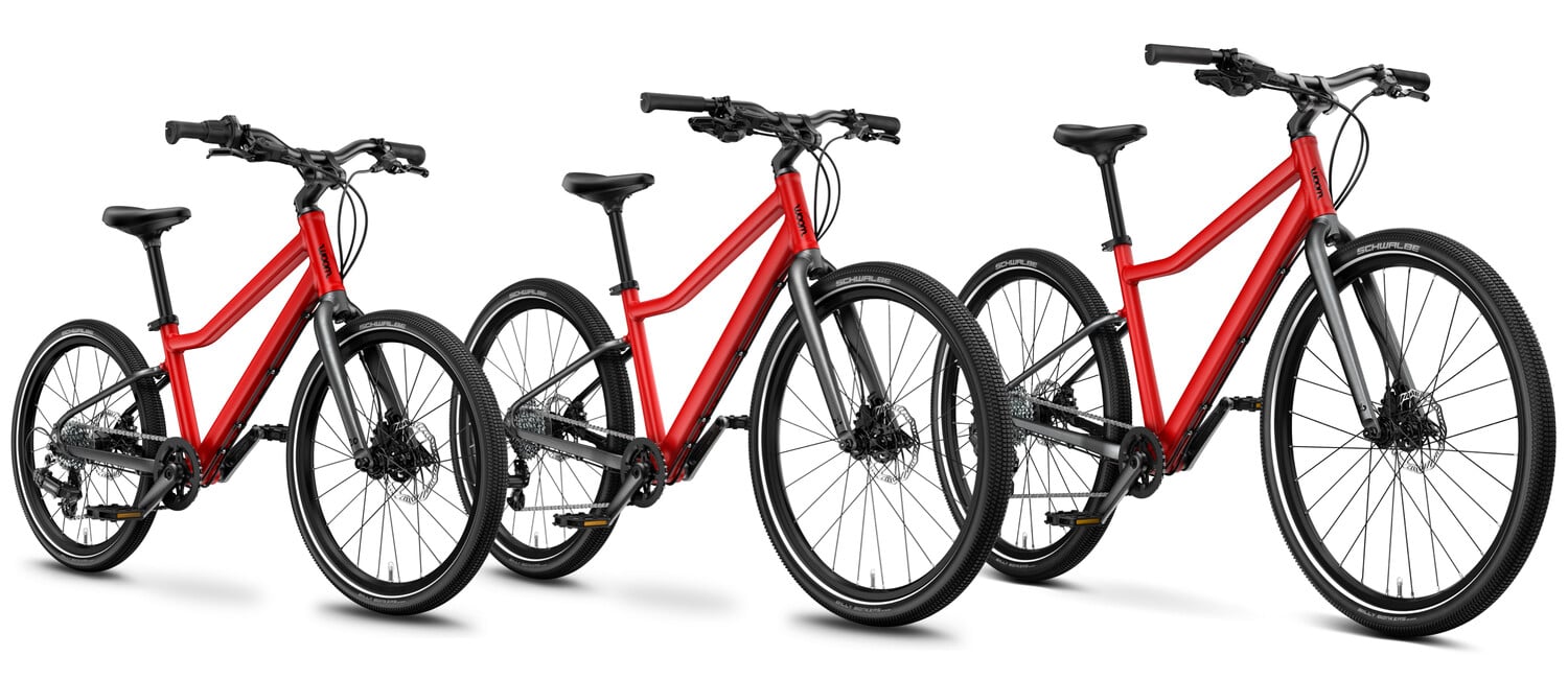 Three red-black woom EXPLORE children's bikes in sizes 4, 5 and 6 lined up alongside each other.