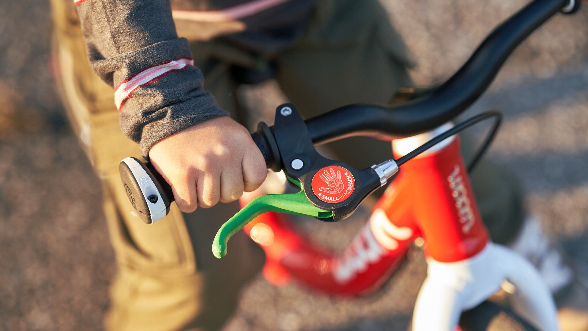 A detailed image of the handlebars and the green brake lever for the rear brake on a red woom balance bike.