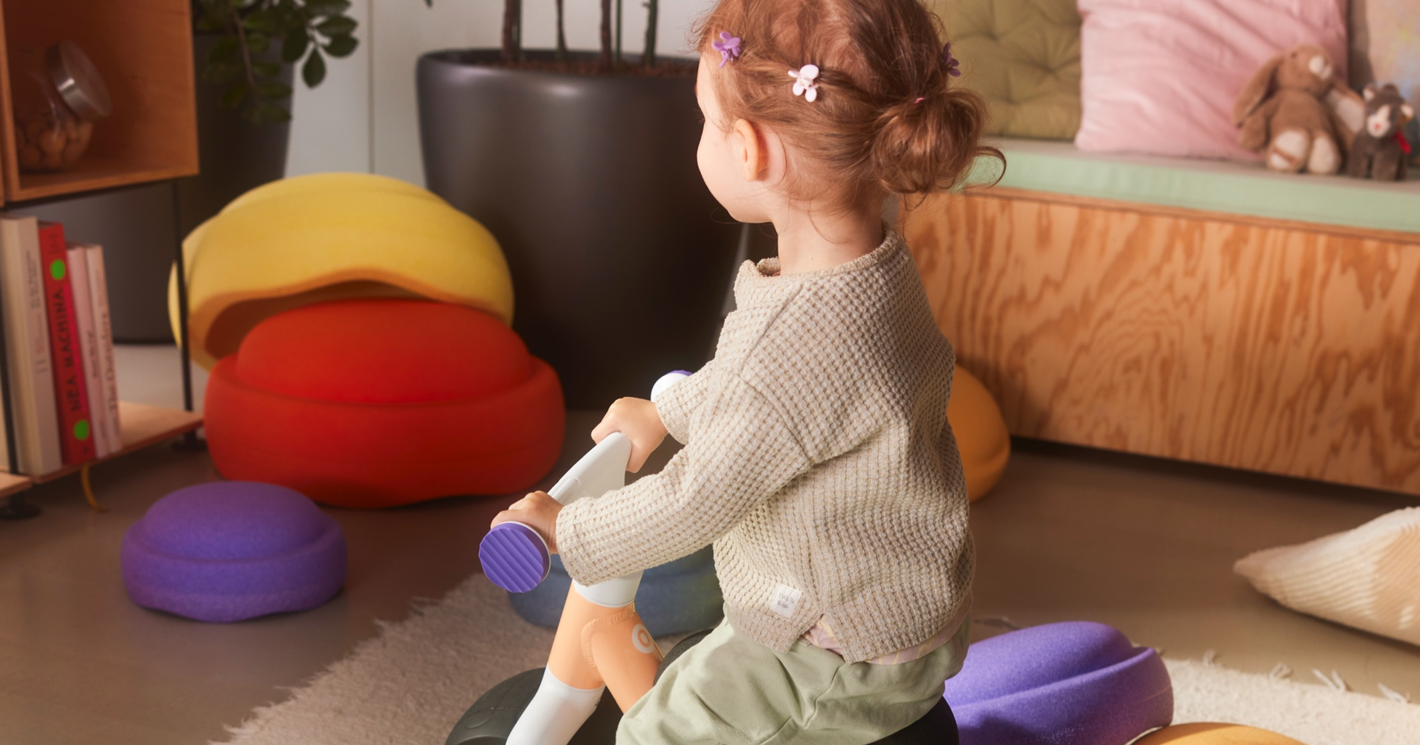 A young child rides a woom WOW in pop peach while surrounded by Stapelstein products
