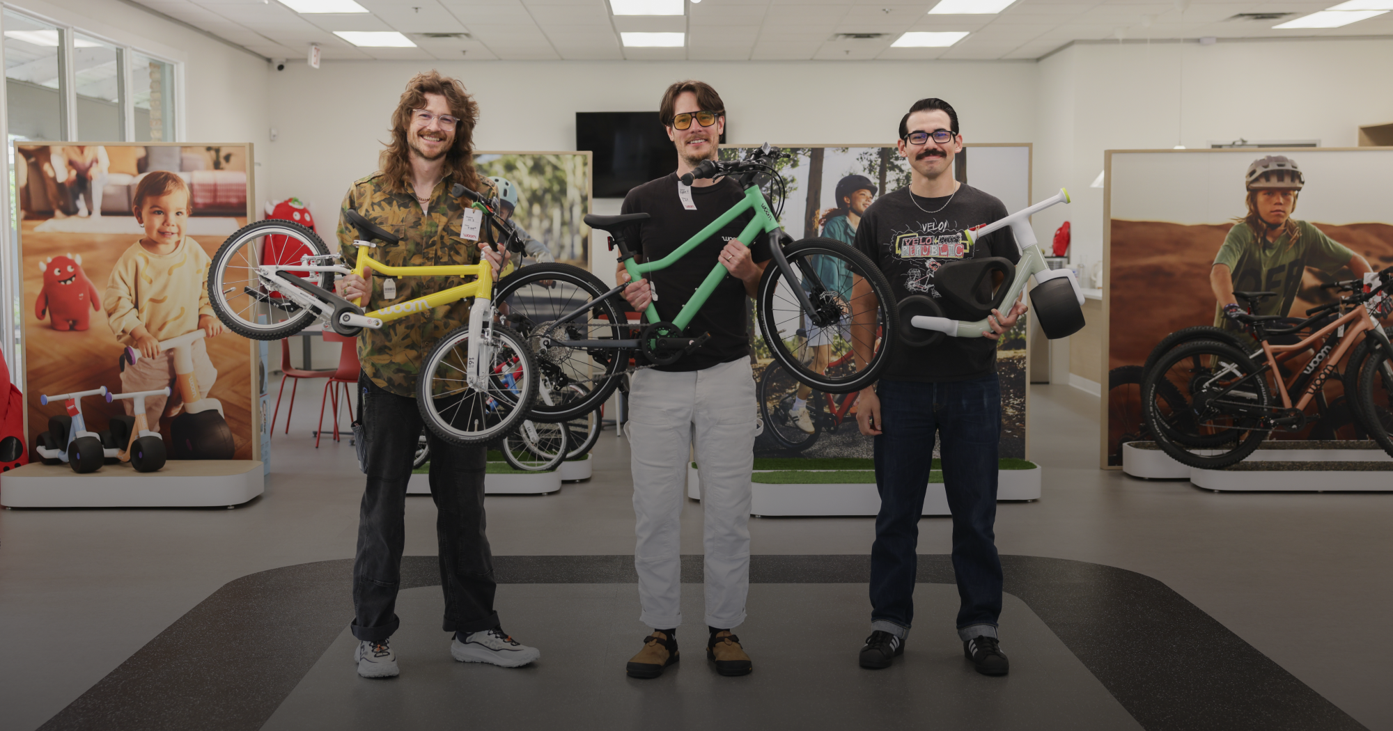 Bike Experts Jackie, Harry, and Matt hold various woom bikes in the showroom.