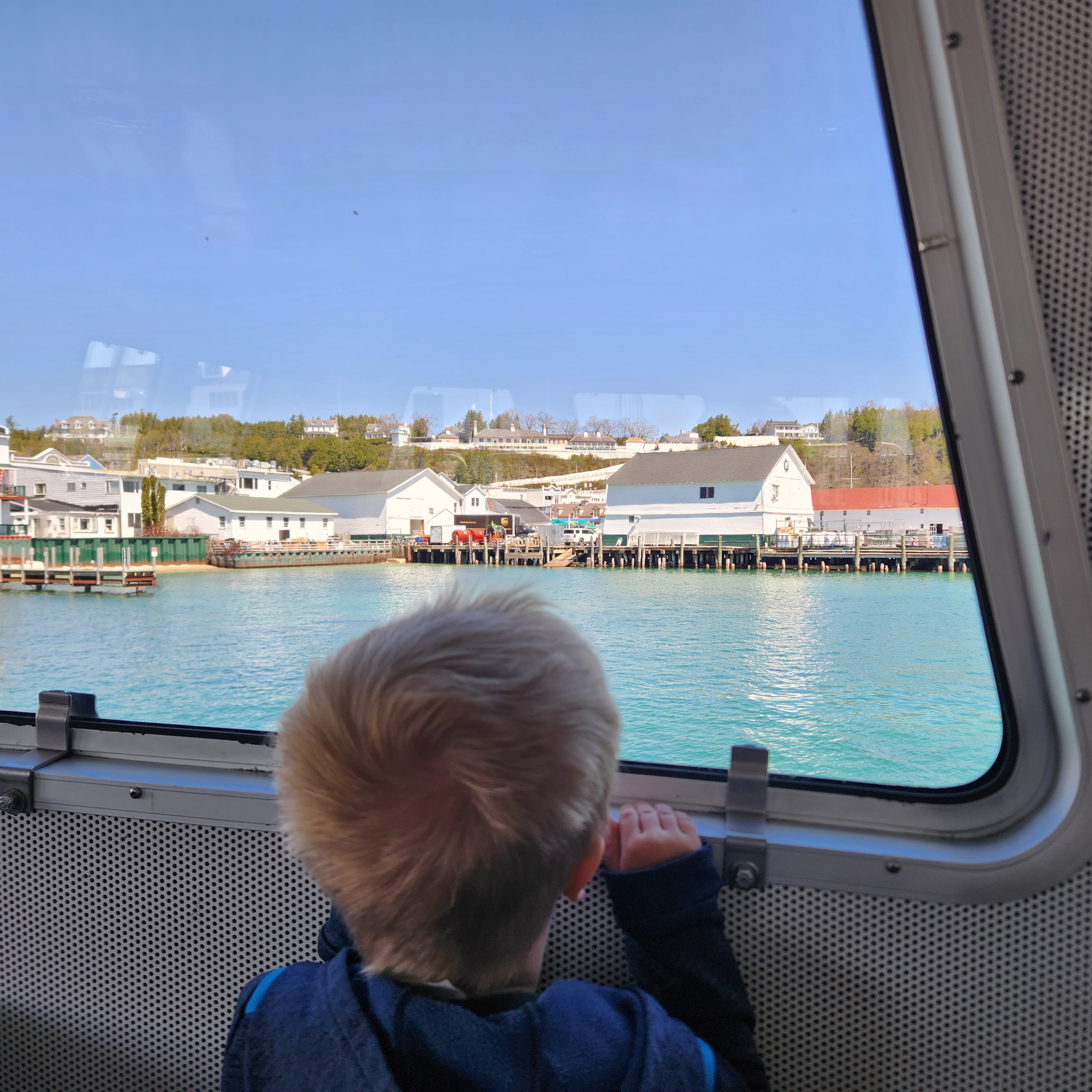 The back of a young boy’s blond head pops up from the bottom of the frame as he watches the docks from the window of the Mackinac Island Ferry.