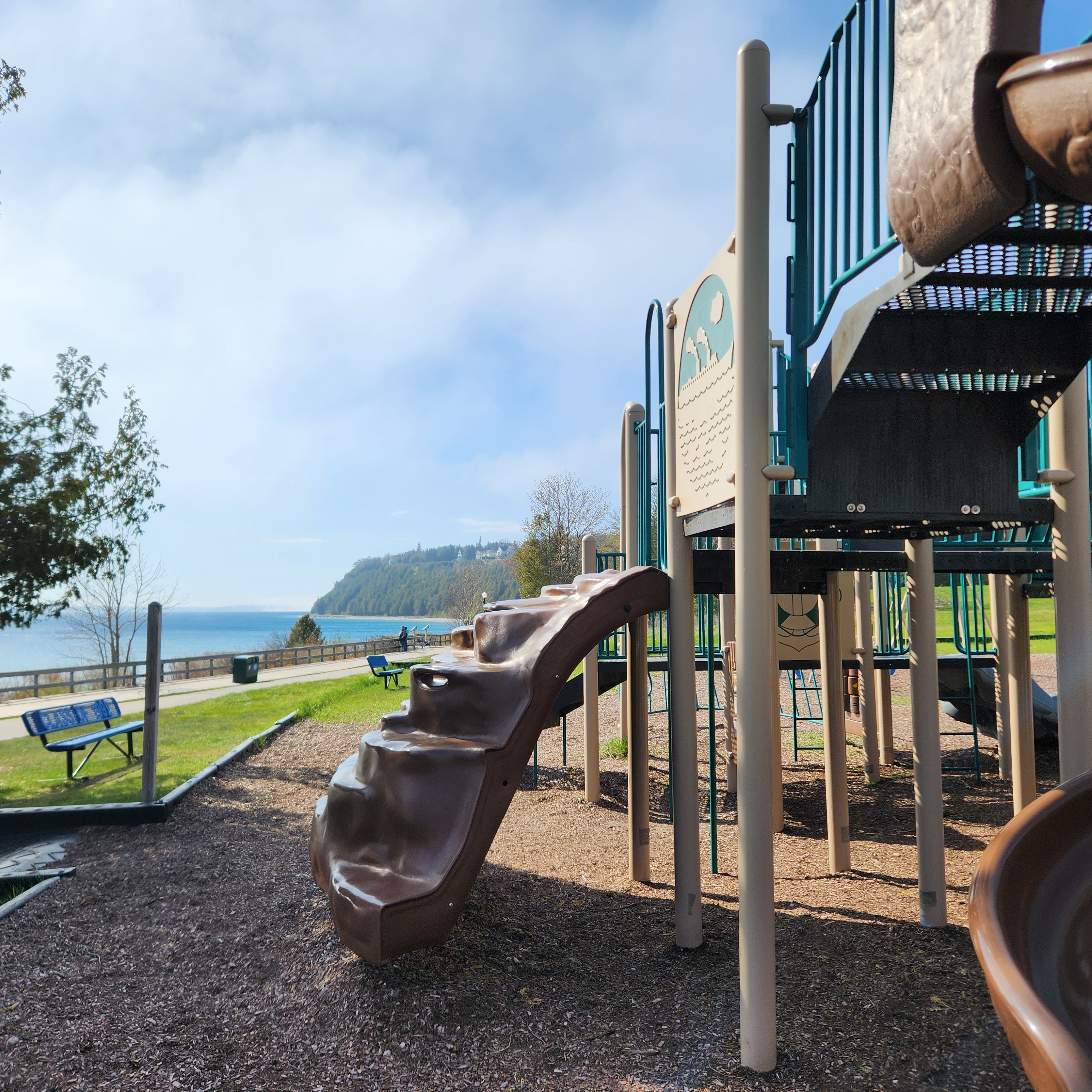 3. A lakeside playground, empty of kids, sits beside blue water. A tree-covered peninsula is visible in the background.