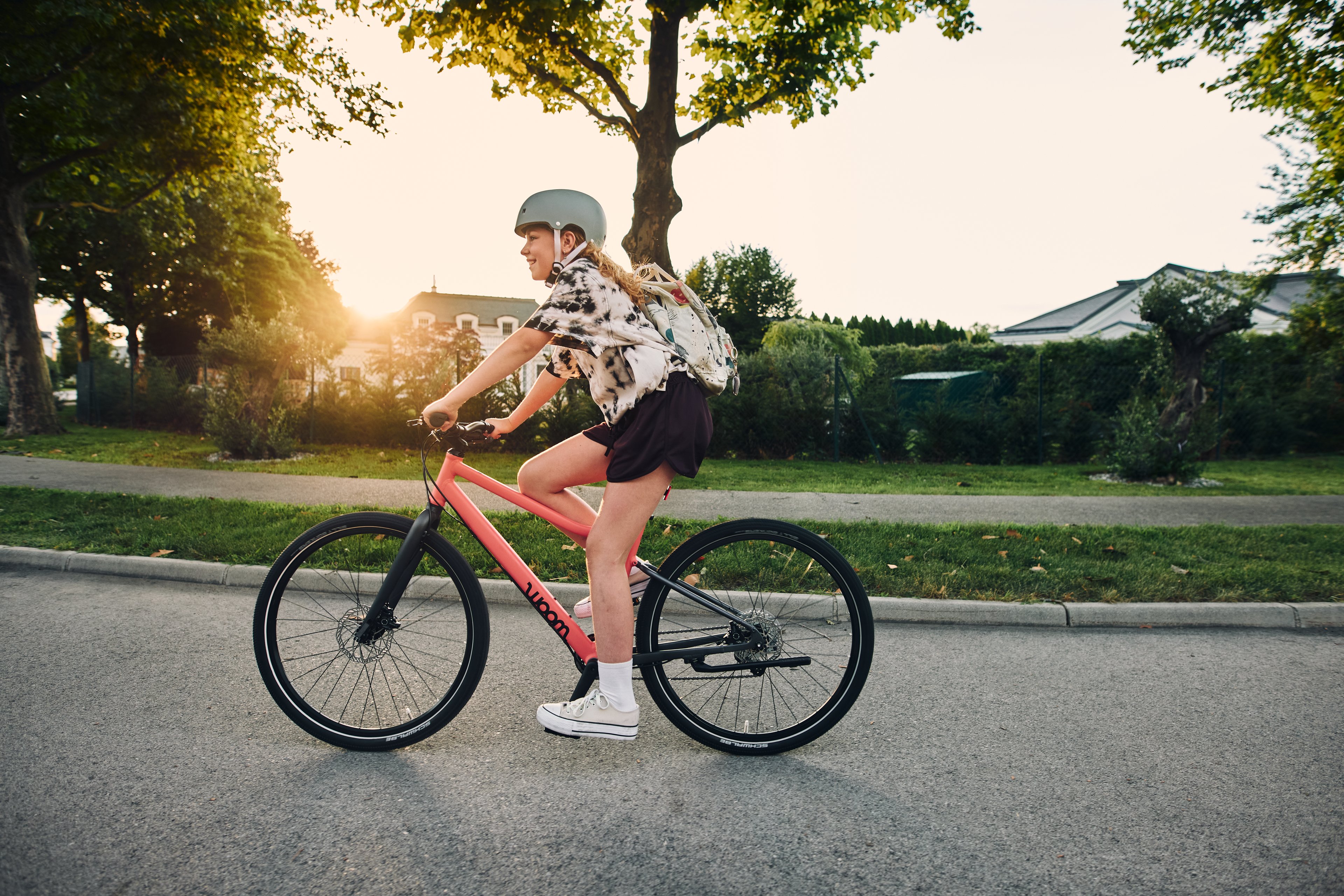 A girl wearing a helmet and a backpack riding an coral woom EXPLORE bike down the street.