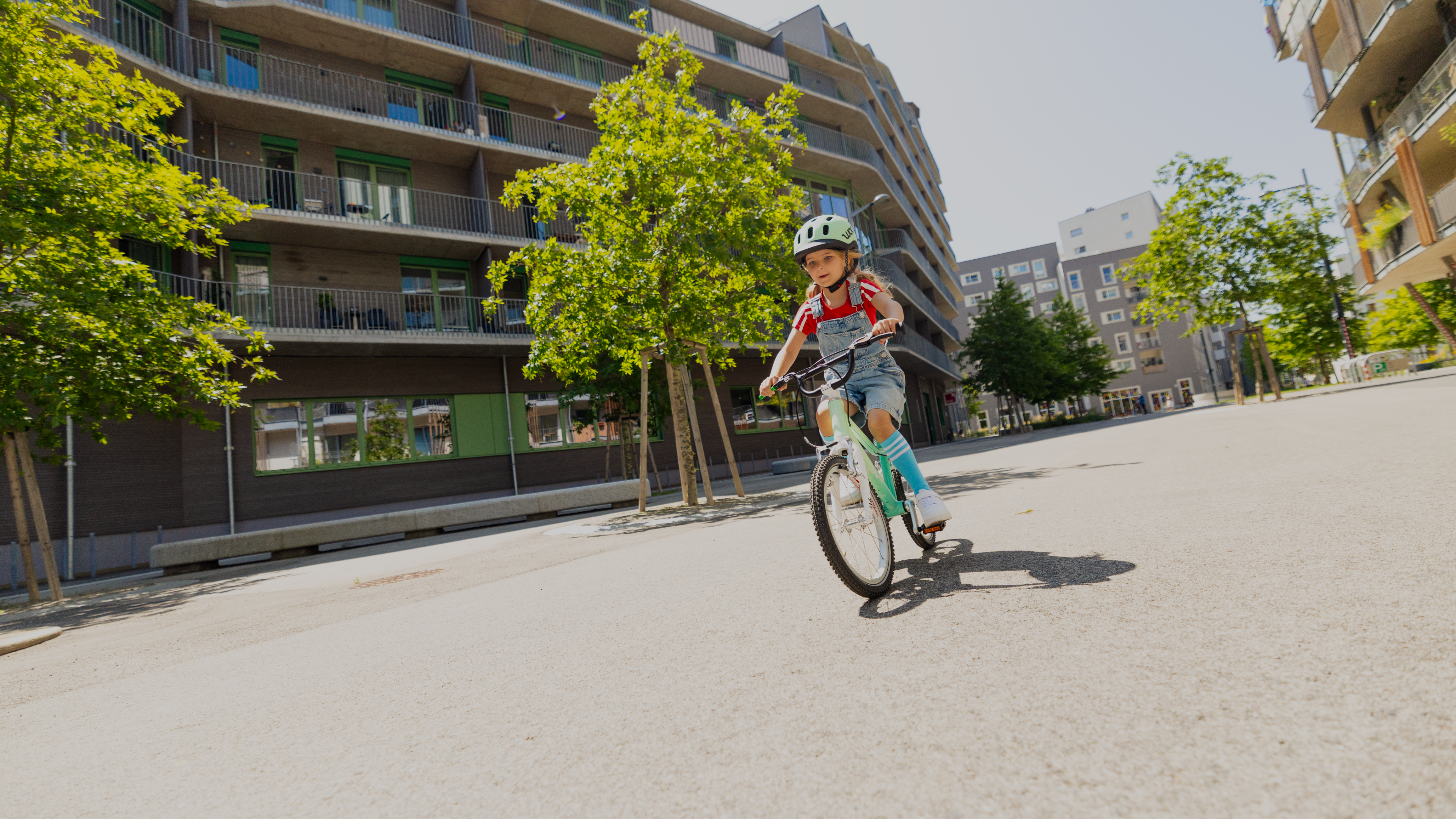 Mädchen mit READY Helm in Mint auf dem Kopf fährt entlang eines Wohnblocks auf dem Fahrrad woom GO in spearmint crush.