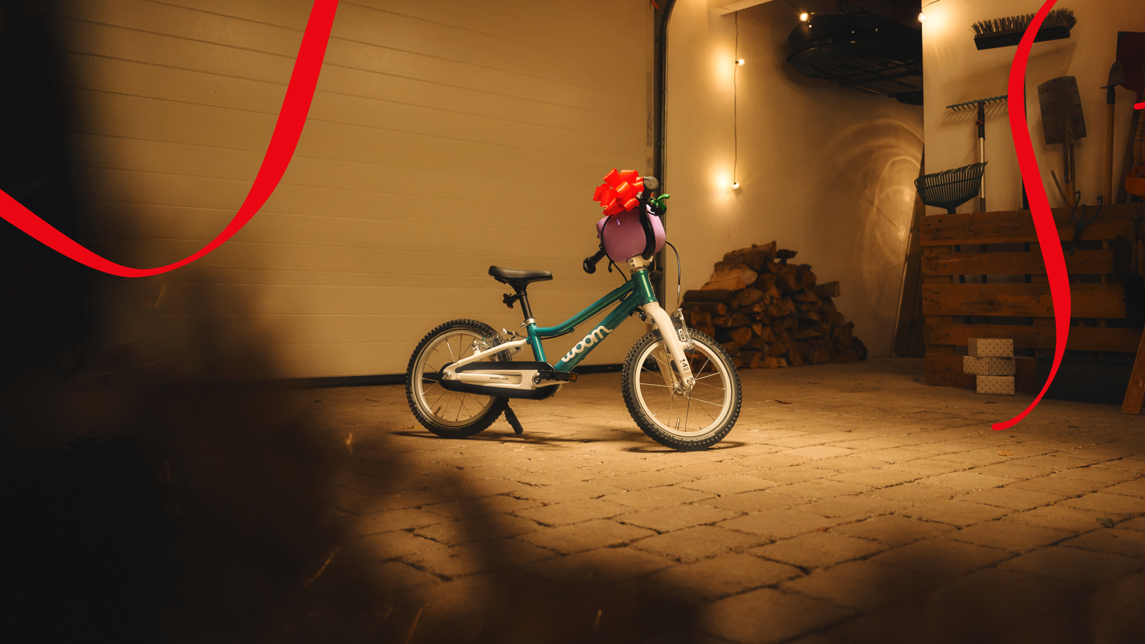 woom GO mit roter Schleife und POP Fahrradkorb, in einer gemütlichen, schwach beleuchteten Garage.