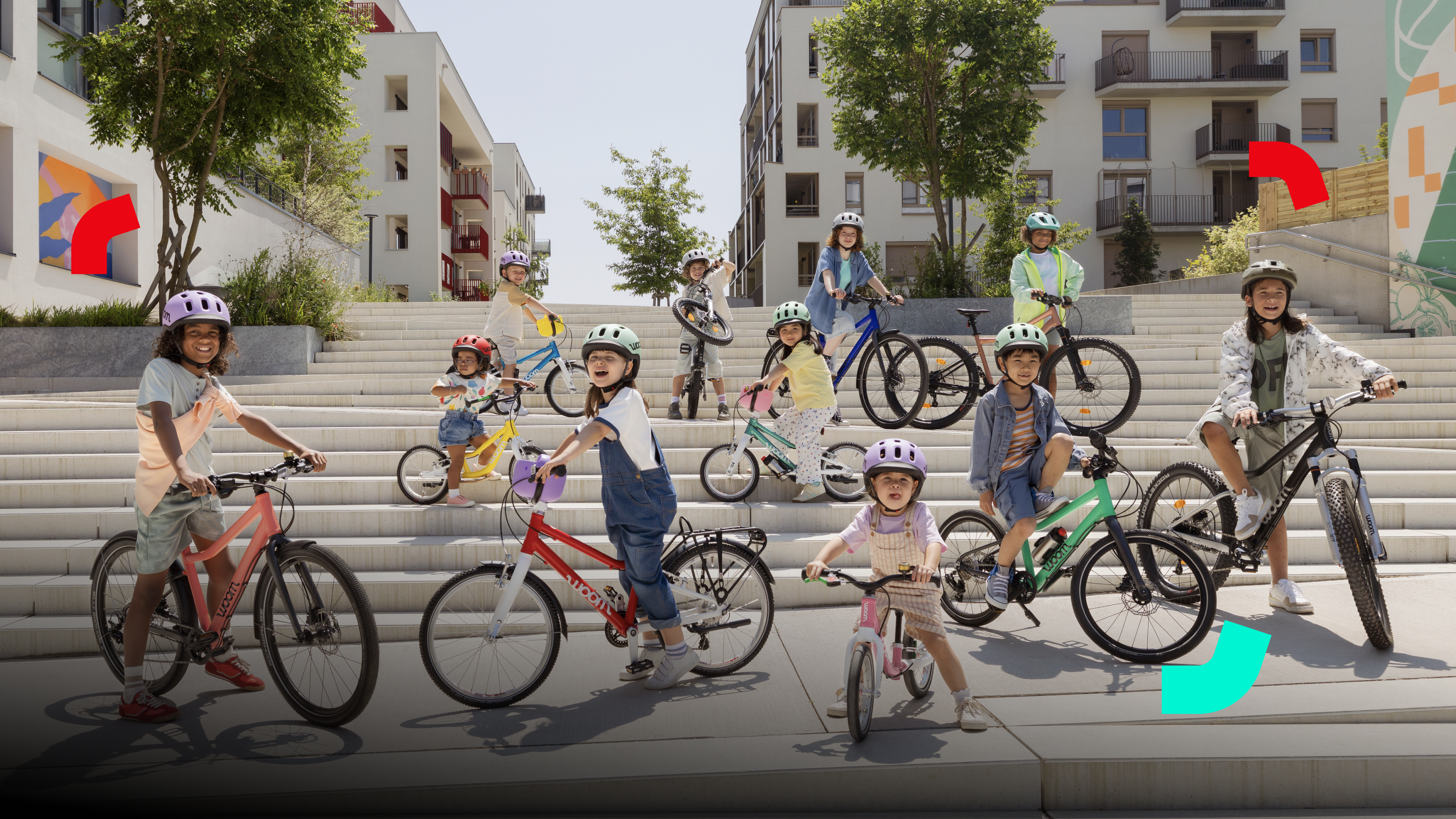 Happy kids on woom bikes wearing woom READY helmets, gathered on wide outdoor steps in a modern residential area.