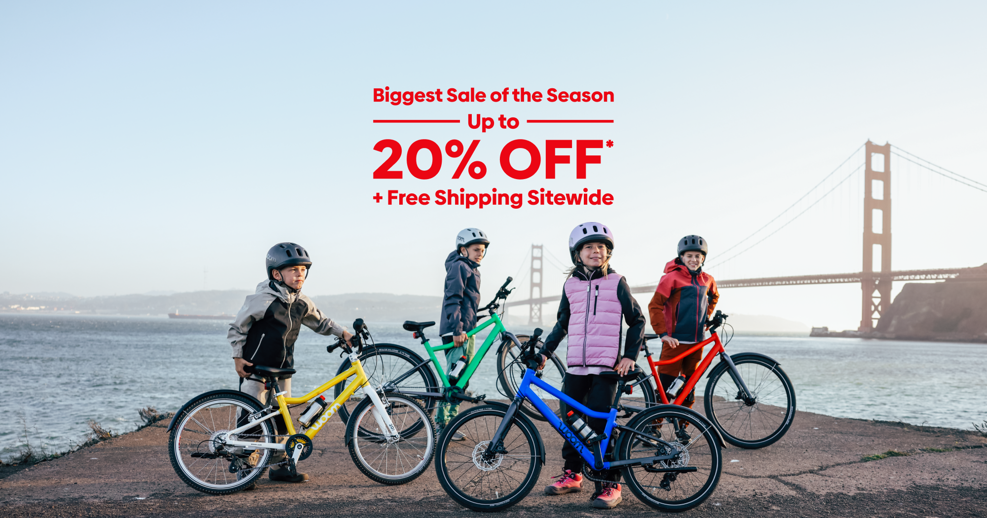 Kids pose with their colorful woom GO and EXPLORE bikes in front of the Golden Gate Bridge on a chilly day. Text over the image reads “Biggest Sale of the Season: Up to 20% Off Plus Free Shipping Sitewide”