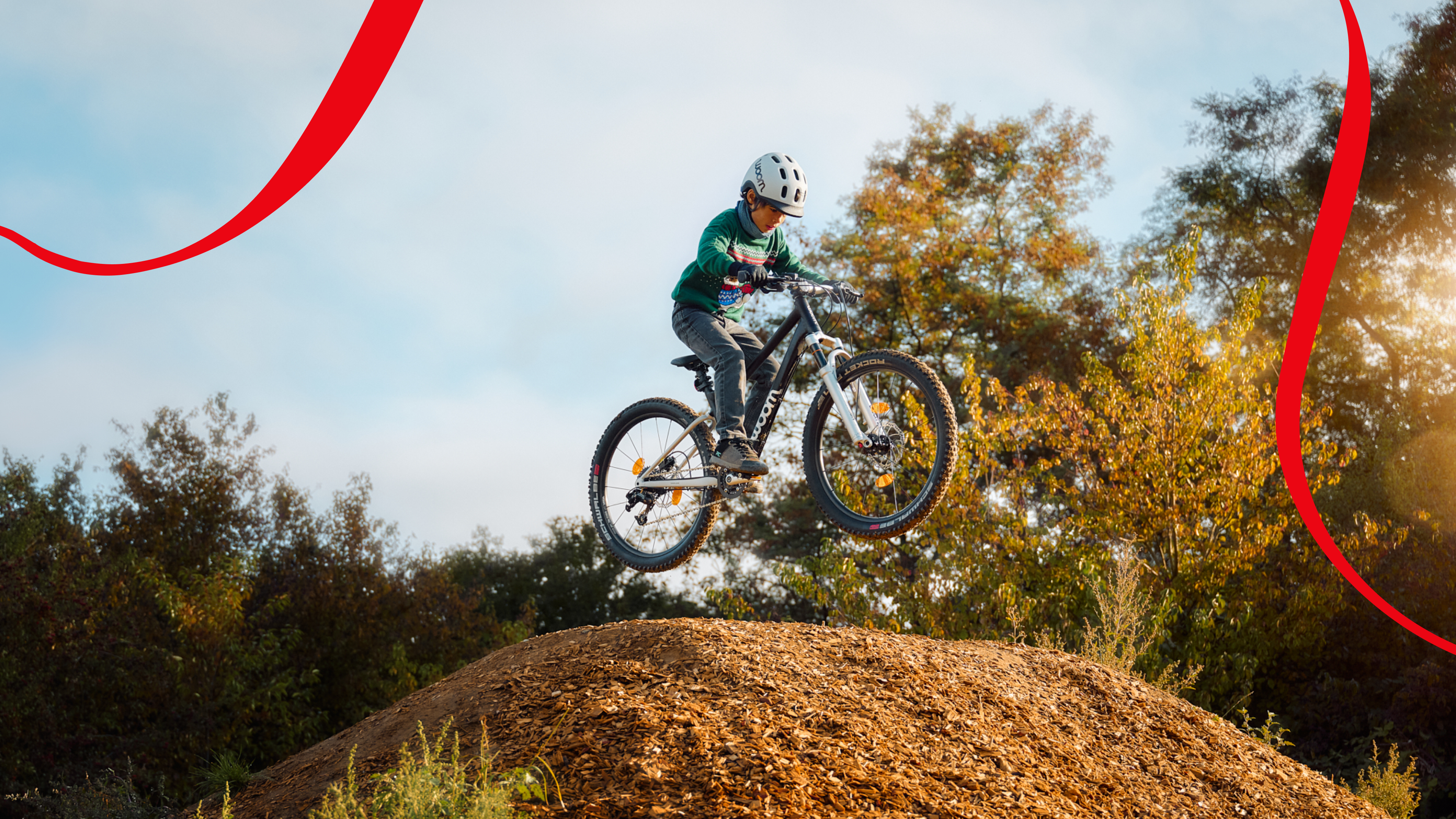 A child with a helmet is jumping over an earth mound with a black woom OFF.