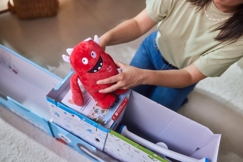 Eine Frau nimmt das Buddy-Plüschtier mit beiden Händen aus der Verpackung des woom WOW Laufrades.