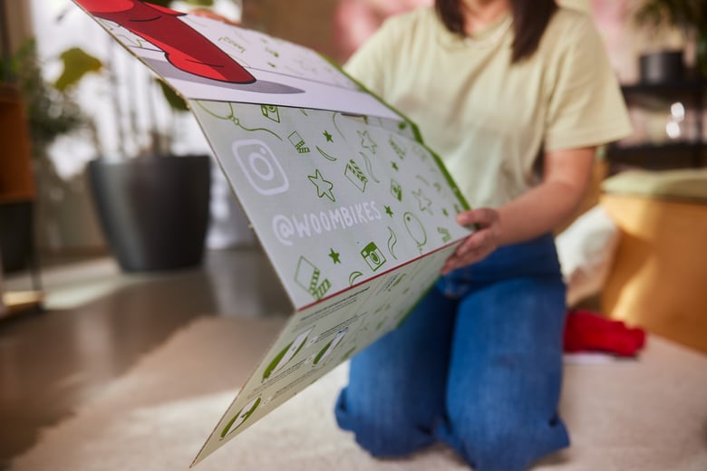 A woman is carefully removing the Buddy photo stand from the woom WOW box with both hands.
