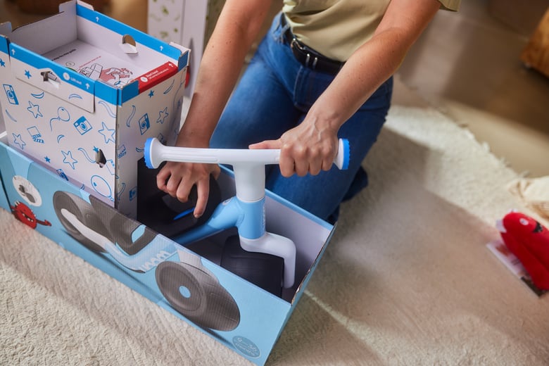 A woman is kneeling in front of the woom WOW box, straightening the handlebars with one hand and holding the saddle with the other.
