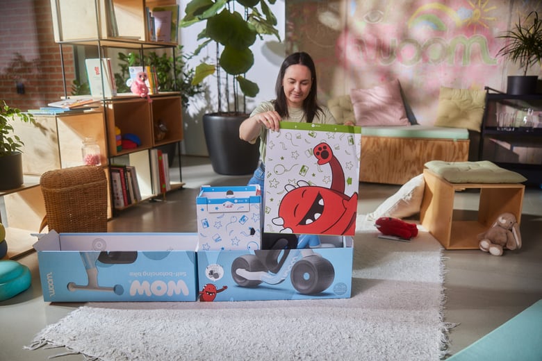 A woman is kneeling behind the light blue woom WOW box in a living room and removing the Buddy photo stand.