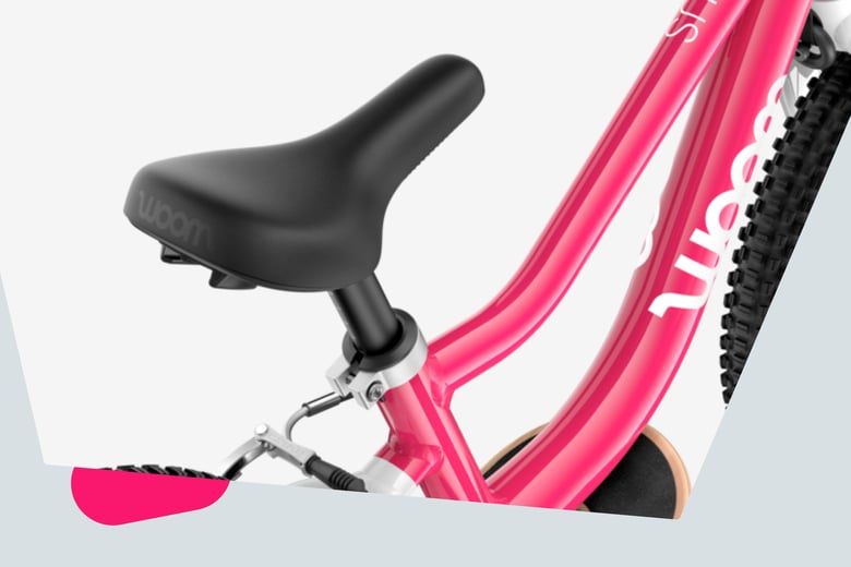 Close-up of the ergonomically profiled bicycle saddle with smooth top surface on a pink woom GO bike