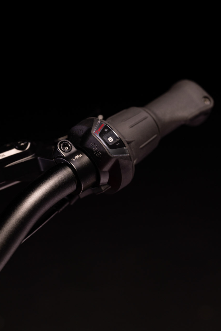 Nahaufnahme des schwarzen woom EXPLORE Lenkers samt schwarzem Shimano Drehschaltgriff mit Ganganzeige.