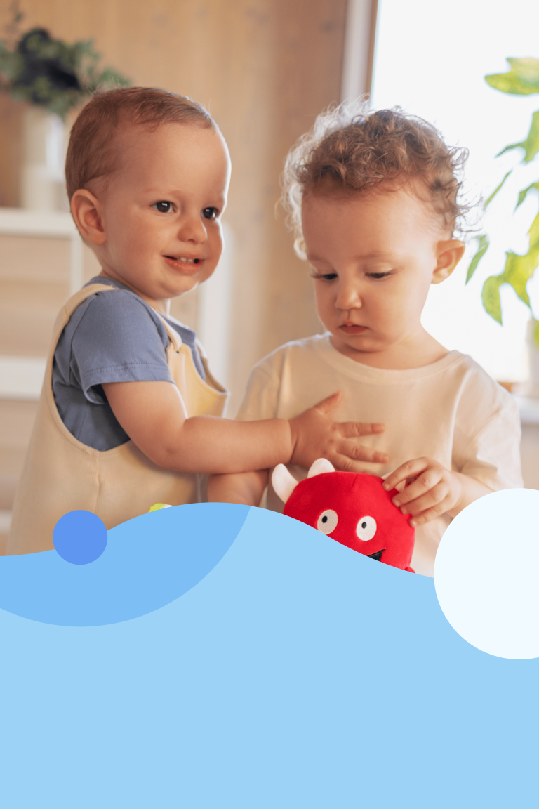 Two toddlers playing with a red Buddy Monster stuffed animal.
