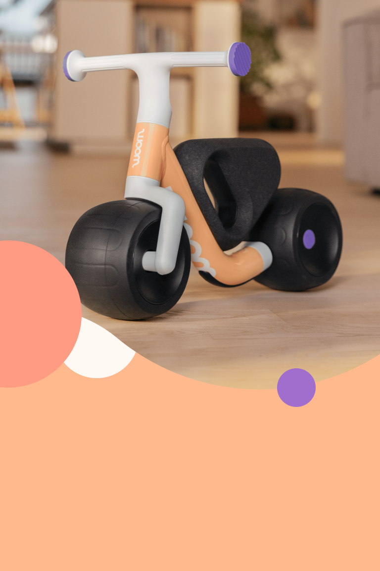 De woom WOW loopfiets in pop peach staat in een lichte kamer. 