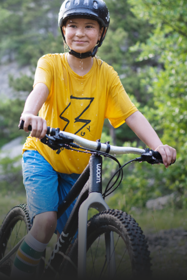 Auf einem schwarzen Kindermountainbike von woom sitzt ein Kind mit schwarzem Fahrradhelm auf dem Kopf.