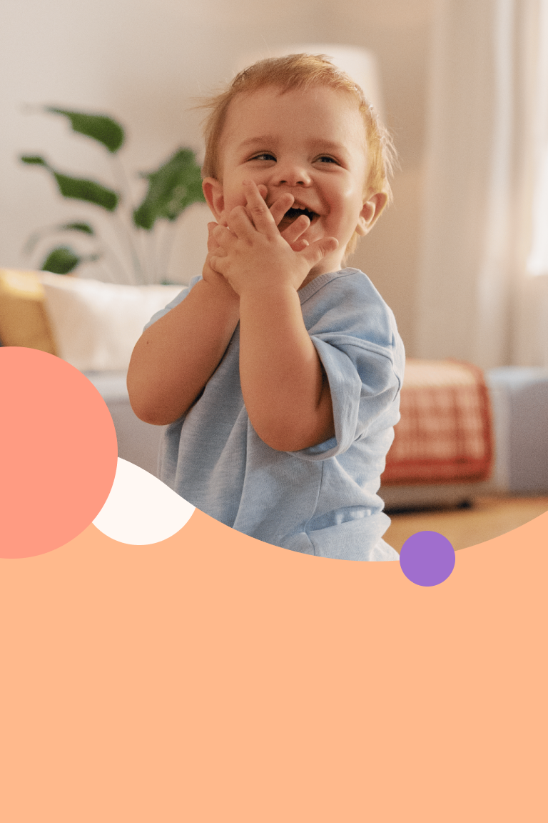 Friendly smiling toddler covering his mouth with his hands out of curiosity.