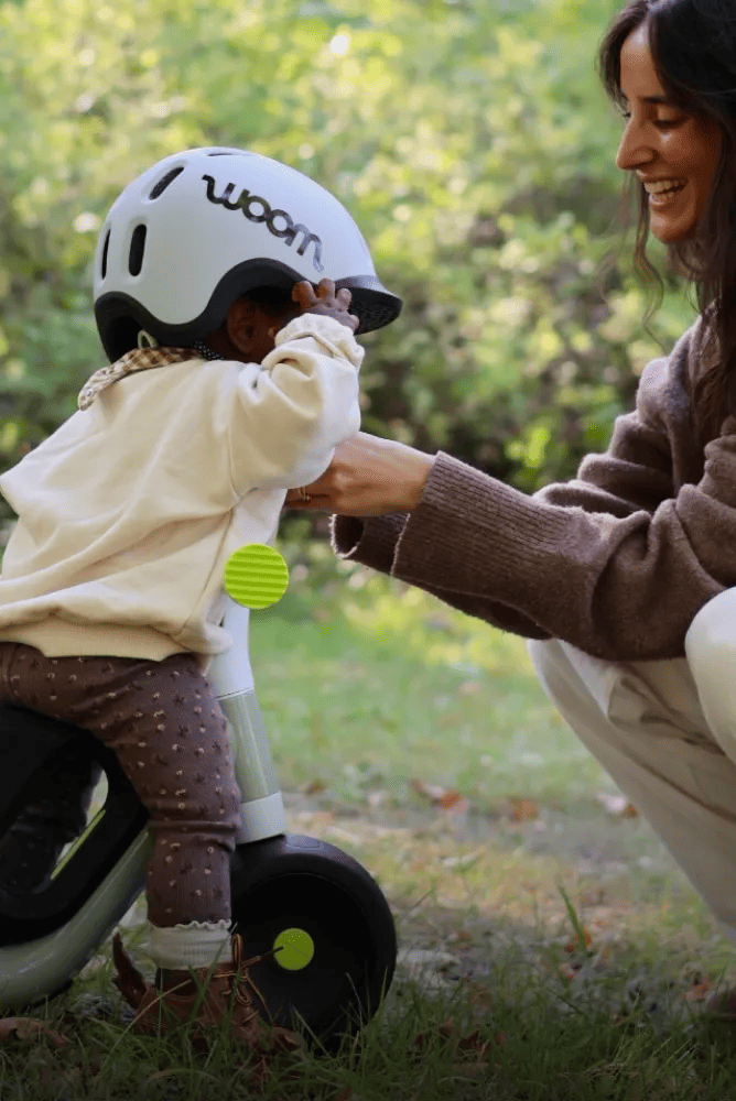 Widok z tyłu dziecka w kasku READY Kids, jeżdżącego na rowerze samobalansującym woom WOW na świeżym powietrzu wraz z mamą.