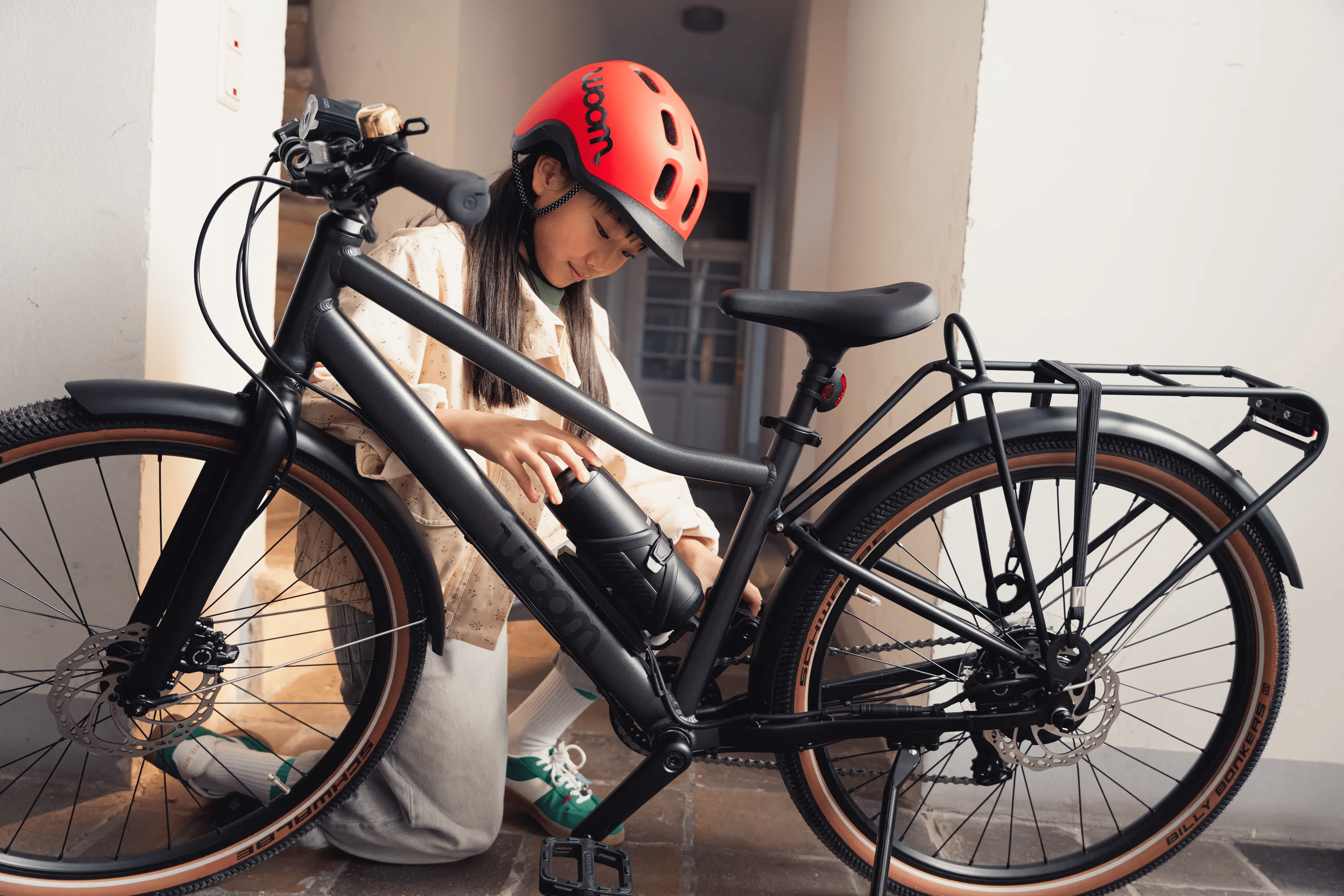 Ein Mädchen schiebt den Akku in die Rahmenhalterung am woom EXPLORE e E-Bike.