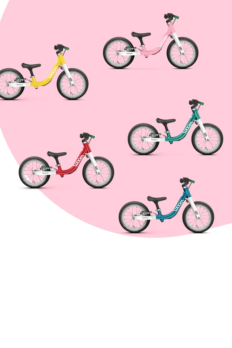 Five woom balance bikes in different colors on a pink background.